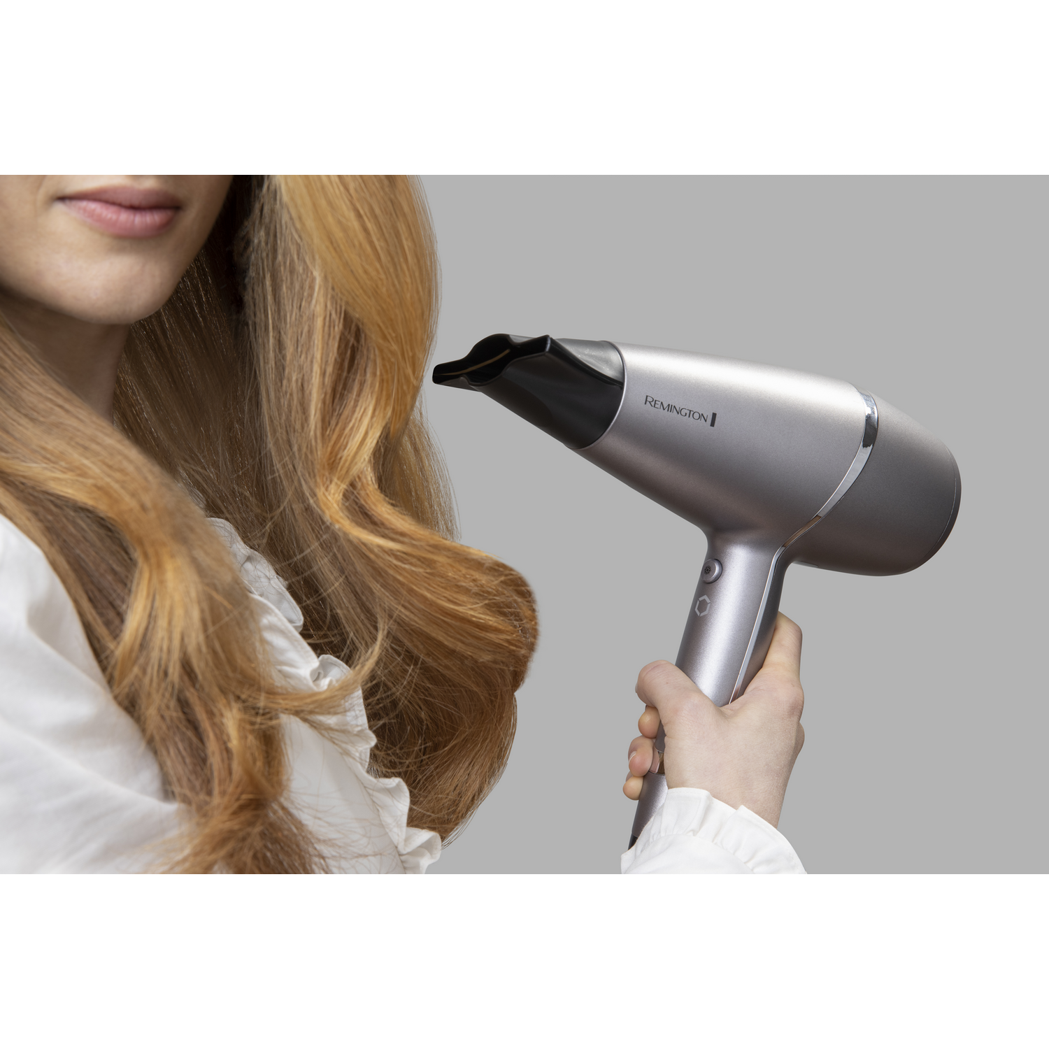 Mujer sosteniendo un secador de pelo plateado. El cabello rubio se está peinando con el secador.