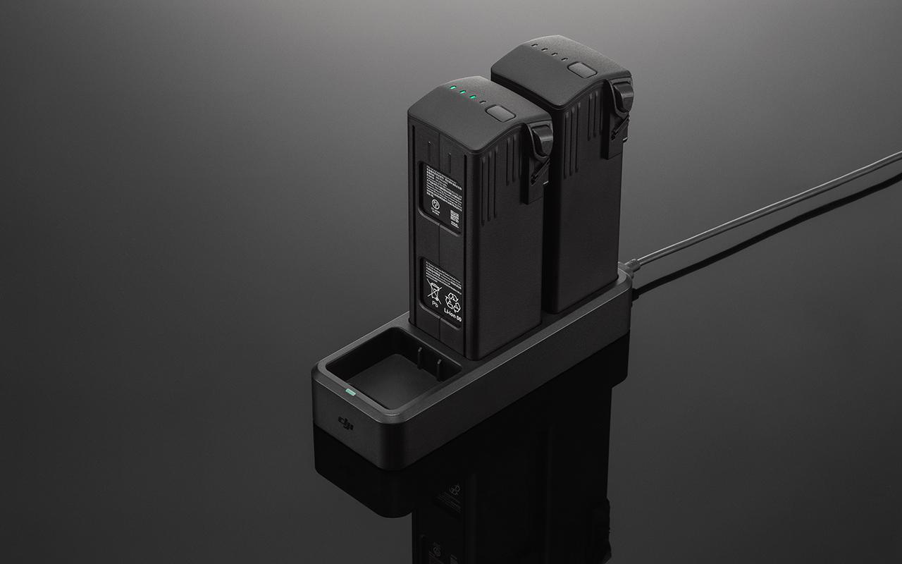 Zwei schwarze Drohnenbatterien auf einer schwarzen Ladestation, auf schwarzem Untergrund.