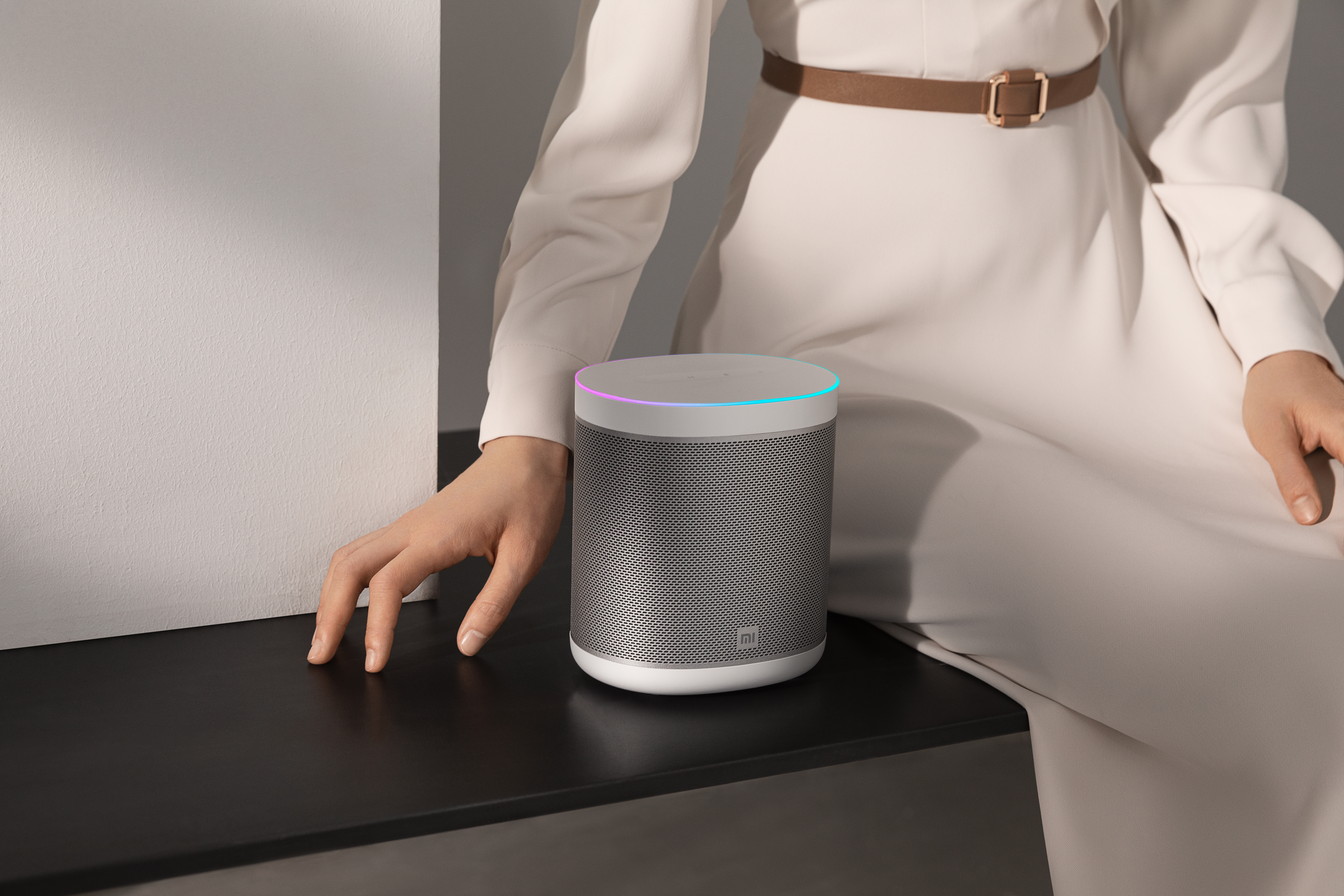 Vrouw met een slimme speaker op een tafel, met een witte muur op de achtergrond.