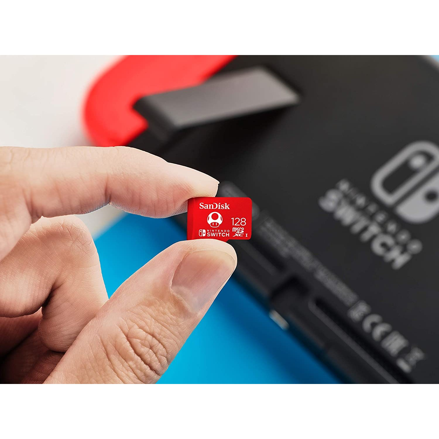 Una persona sostiene una tarjeta microSD SanDisk roja de 128 GB junto a una consola Nintendo Switch.