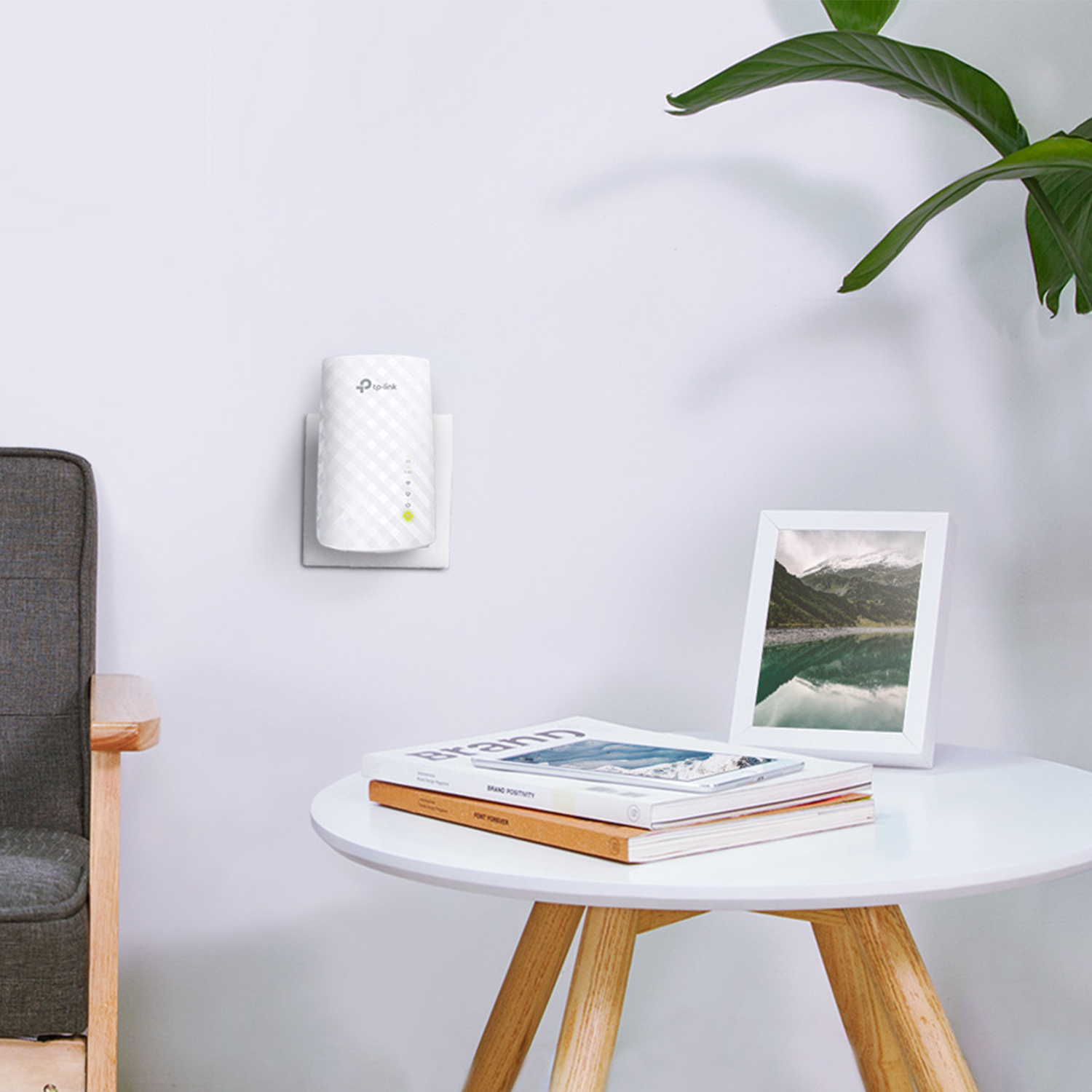 Extensor Wi-Fi TP-Link blanco enchufado a la pared. Mesa con libros y un marco al frente.