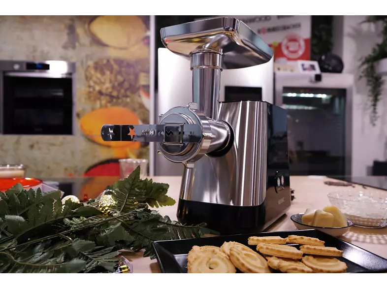 Scène de cuisine avec un hachoir. Des biscuits, une fougère et un bol d'ingrédients sont sur la table.