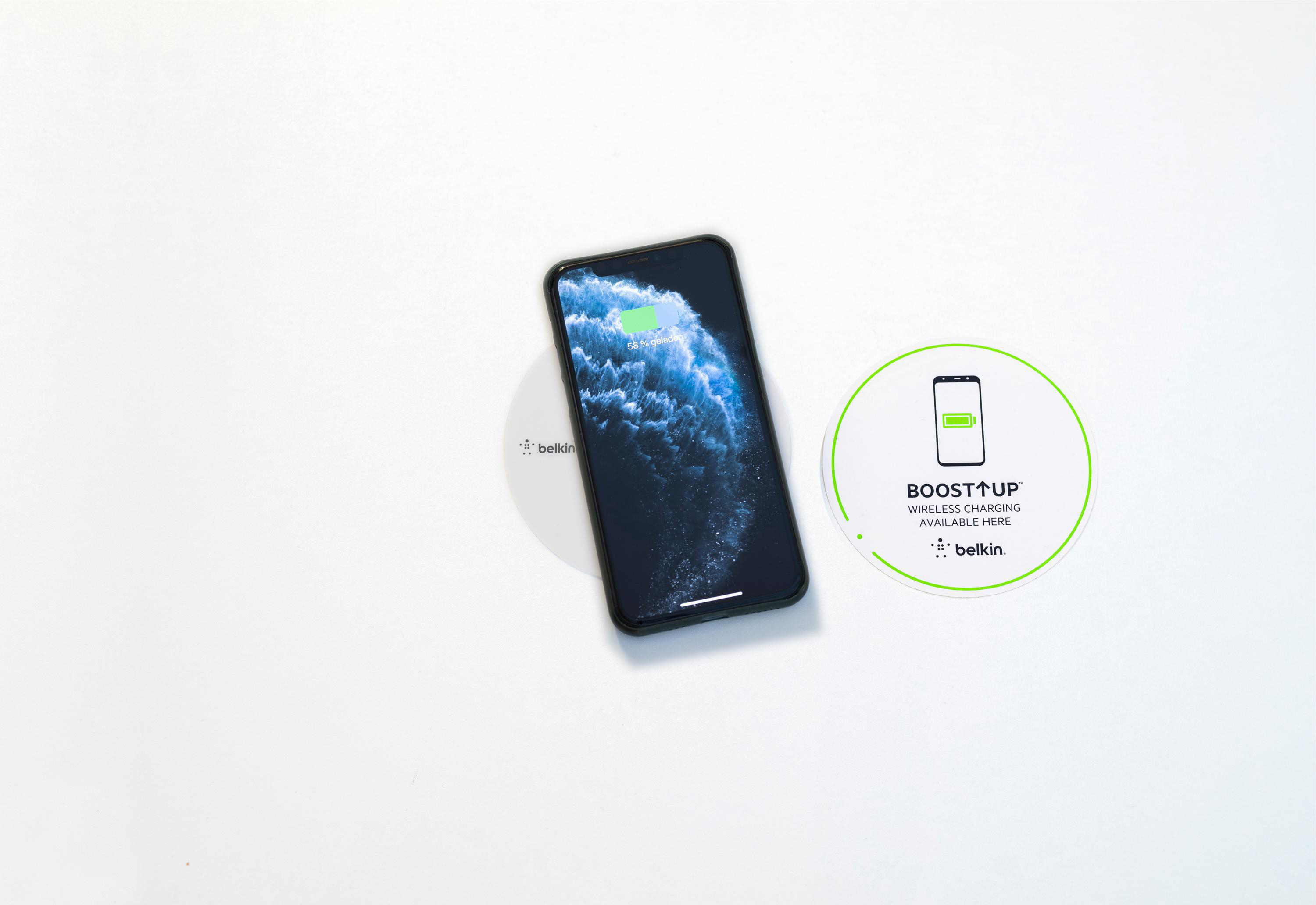 Ein Telefon lädt drahtlos auf einer weißen Oberfläche. Es gibt zwei Ladepads mit Text.