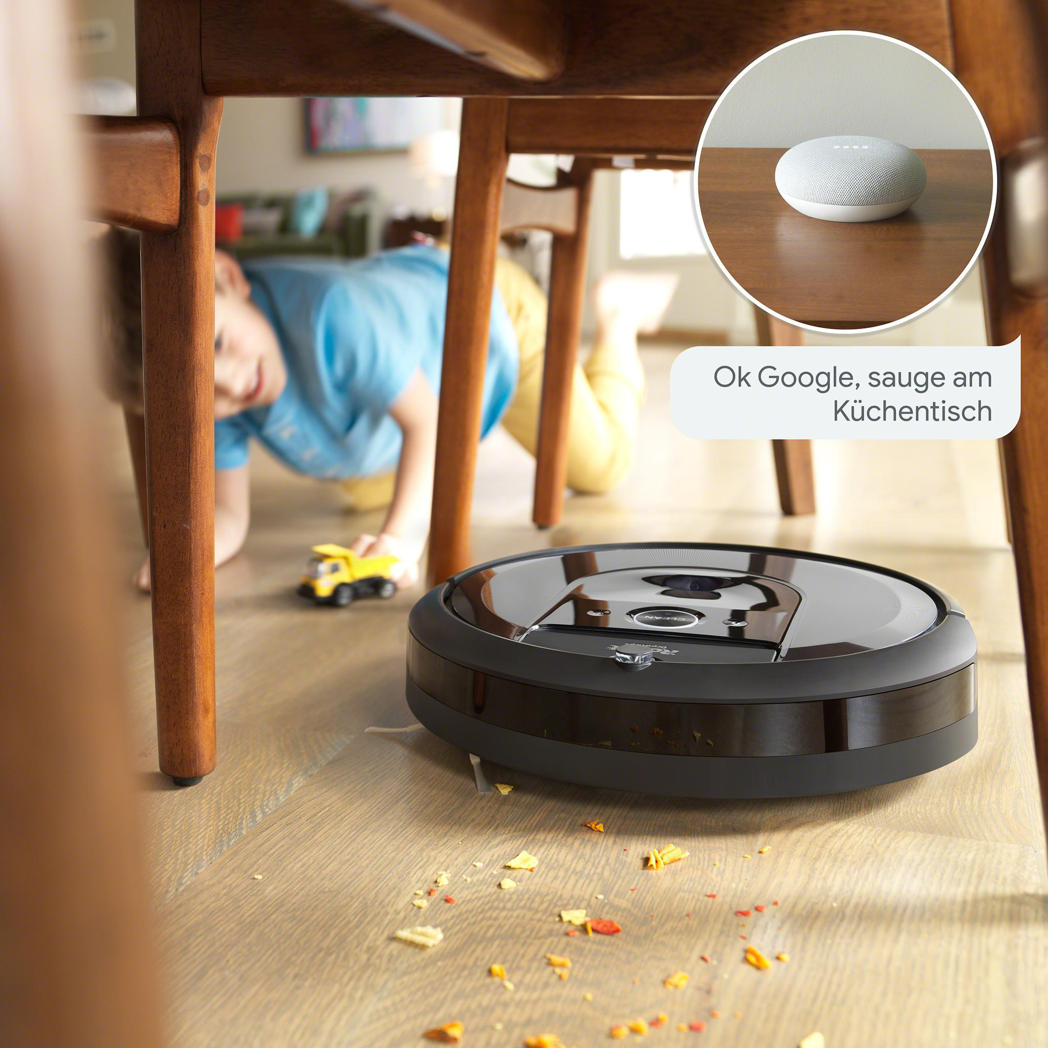 Ein Roboter-Staubsauger reinigt einen Holzboden. Ein Kind spielt in der Nähe. Sprechblase: Ok Google, sauge am Küchentisch.