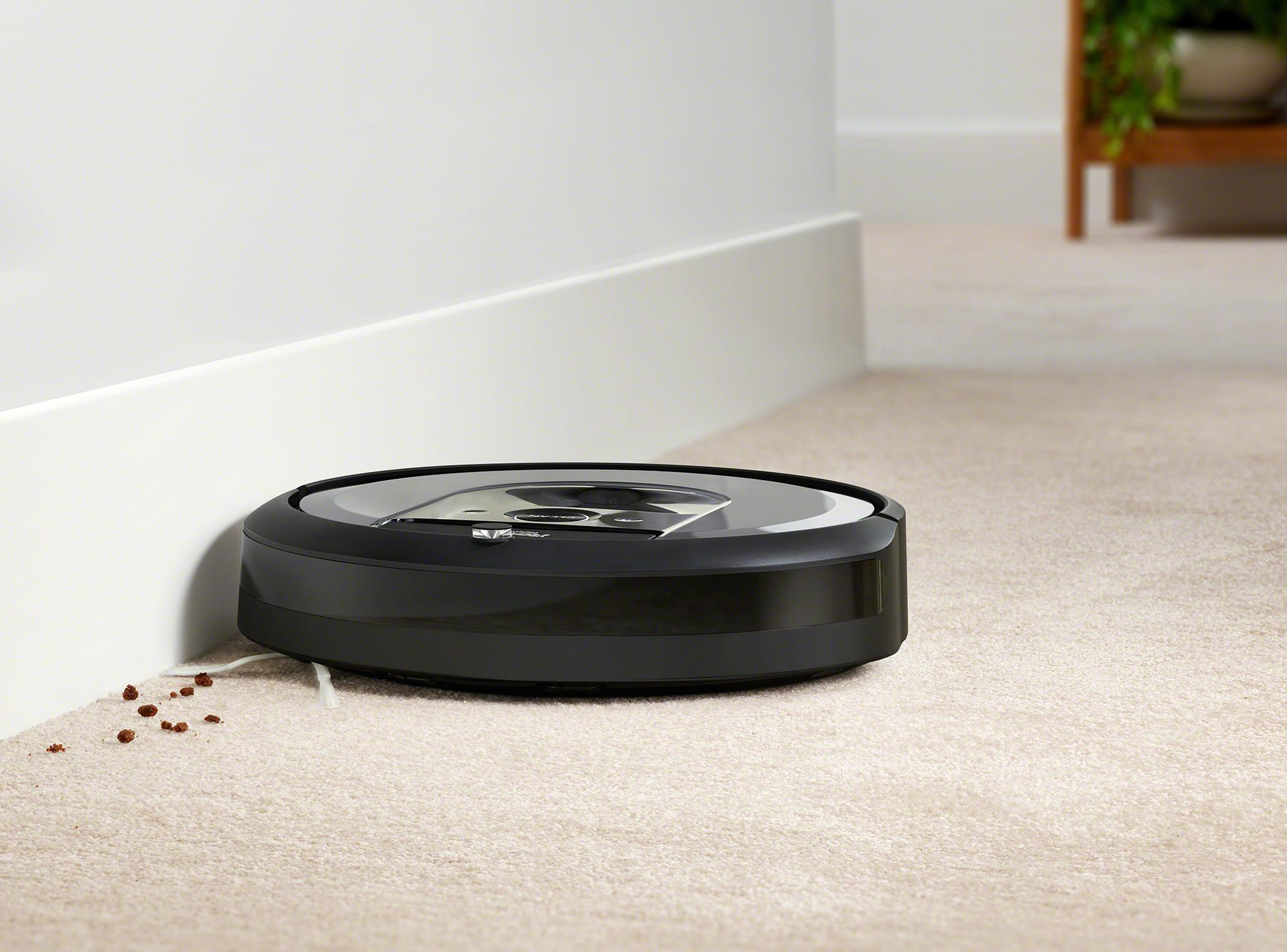 Ein Roboter-Staubsauger reinigt einen Teppich neben einer Wand.