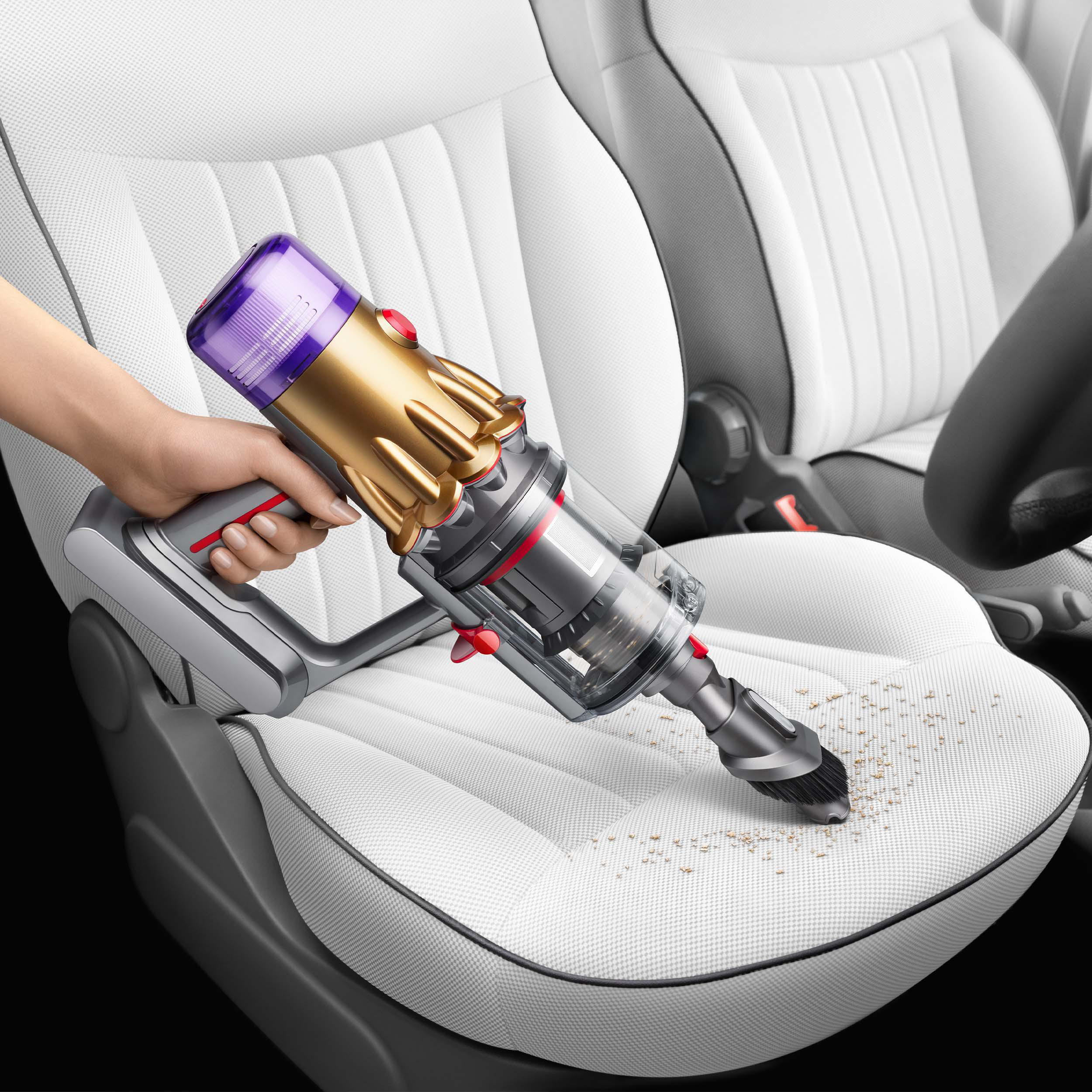 Eine Hand, die einen gold-violetten Handstaubsauger auf einem weißen Autositz benutzt.