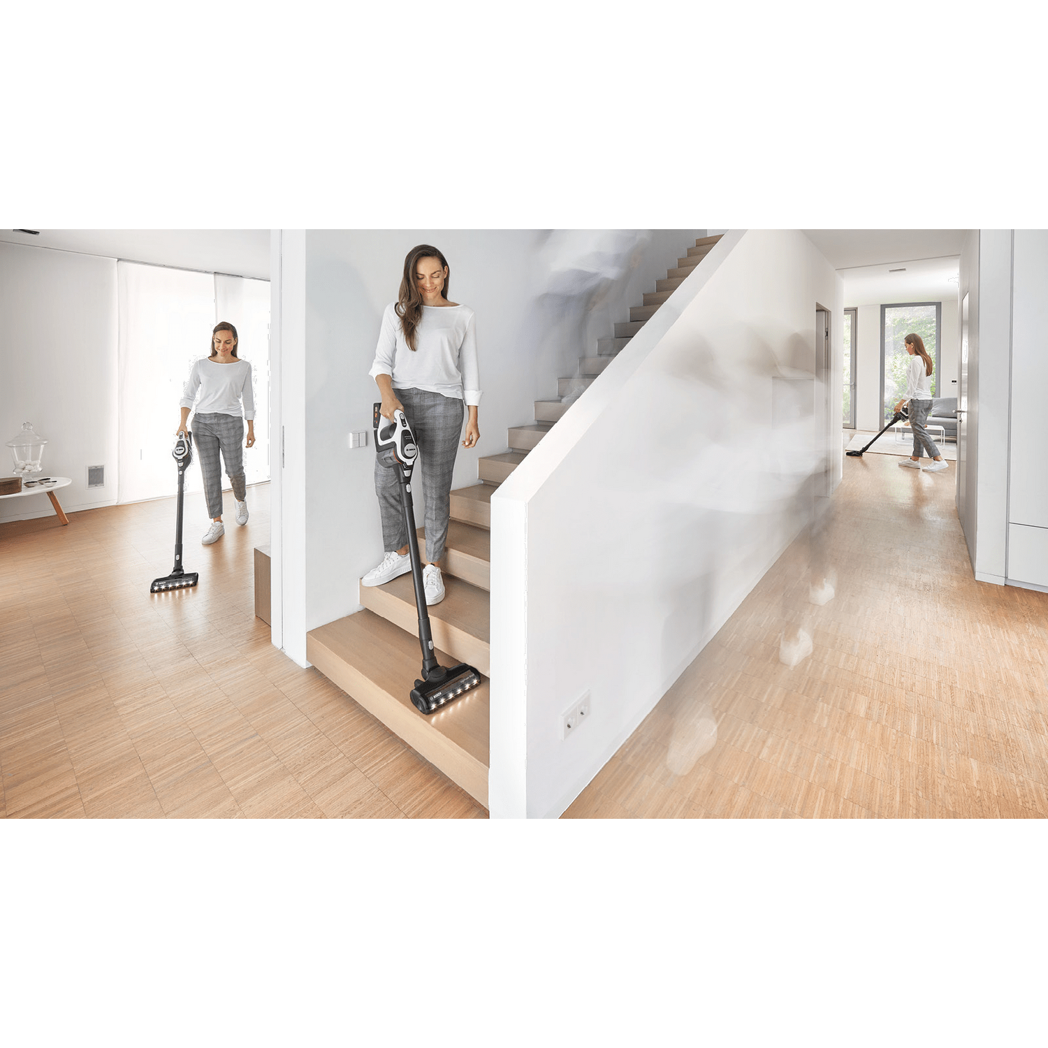 Tres mujeres aspirando una casa. Una en las escaleras, dos en el pasillo. Suelo de madera.