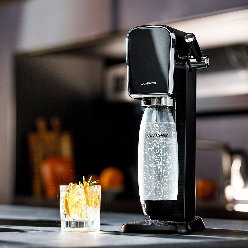 Une machine à soda noire avec un verre de boisson sur un comptoir, des tranches d'orange et du romarin.