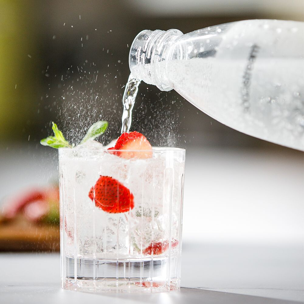 Un verre d'eau gazeuse avec de la glace et des fraises. De l'eau est versée dans le verre à partir d'une bouteille.