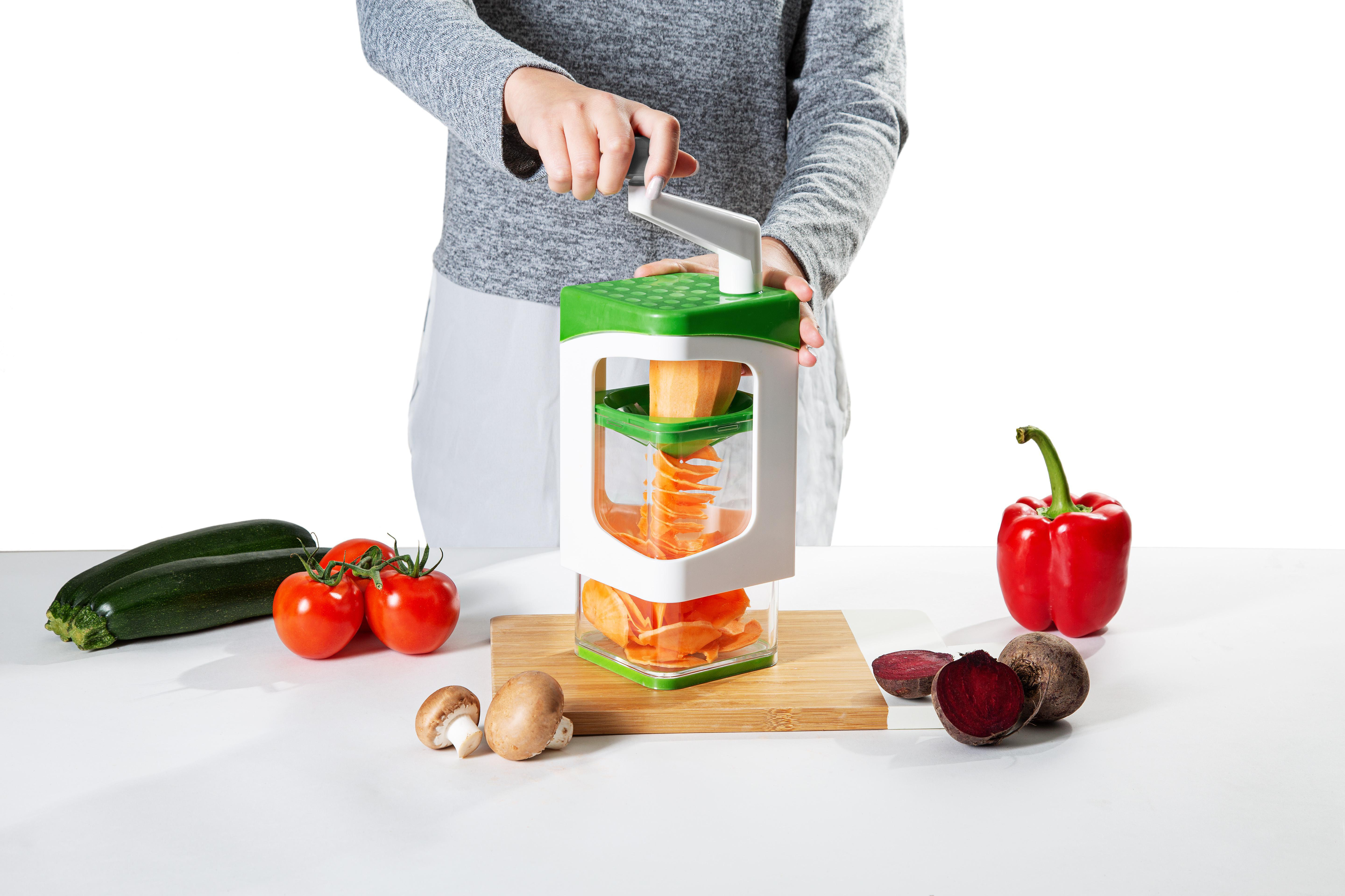 Person verwendet einen Gemüsespiralschneider. Zucchini, Tomaten, Pilze, Rote Bete. Rote Paprika. Weißer Hintergrund.
