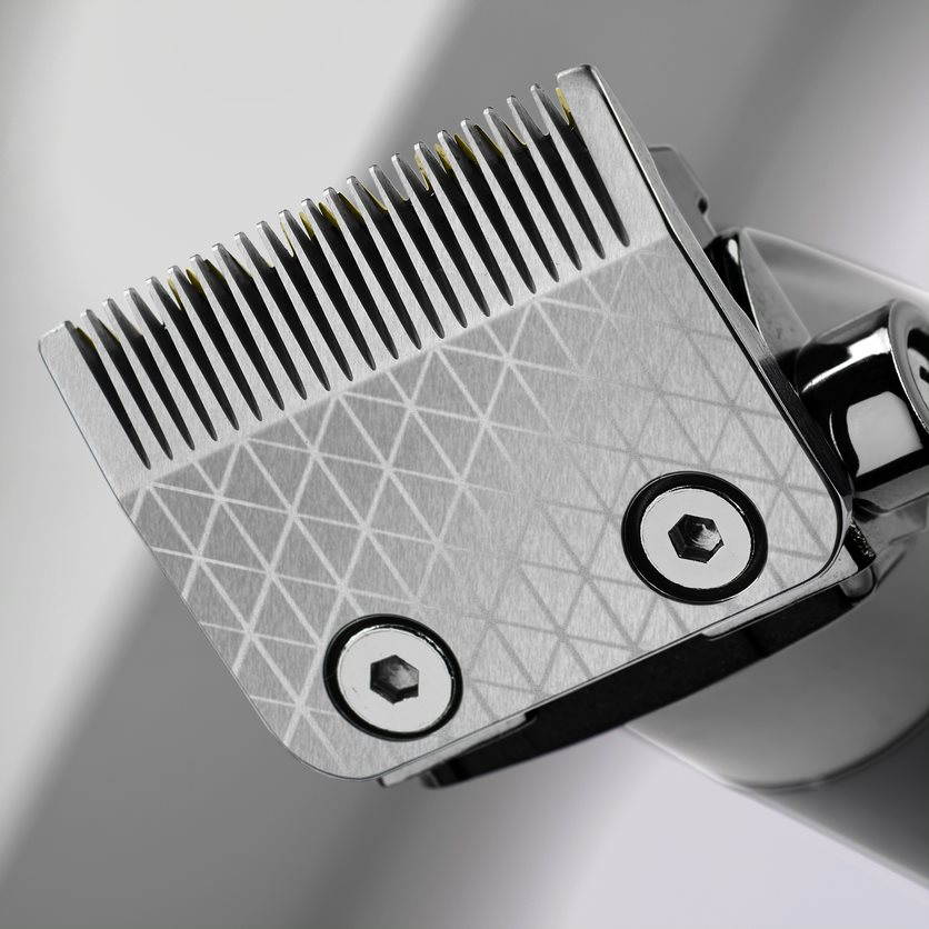 Close-up of a hair clipper blade, silver, with a patterned surface, and two screws.