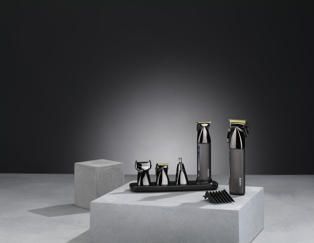 Set of barber tools on a platform: trimmers, clippers, and accessories, on a gray backdrop.