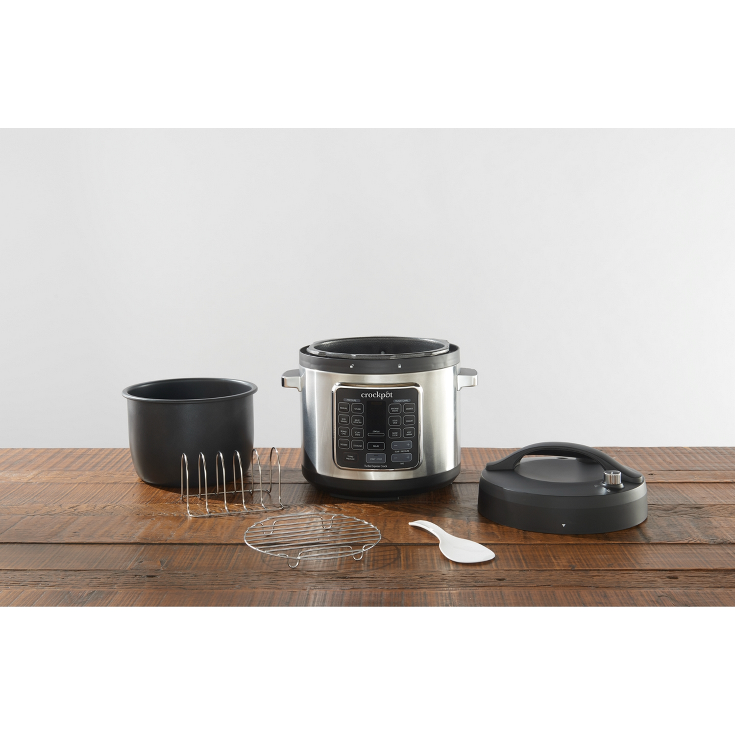 Crockpot y accesorios en una mesa de madera. Incluye olla interna, rejilla, cuchara, tapa.