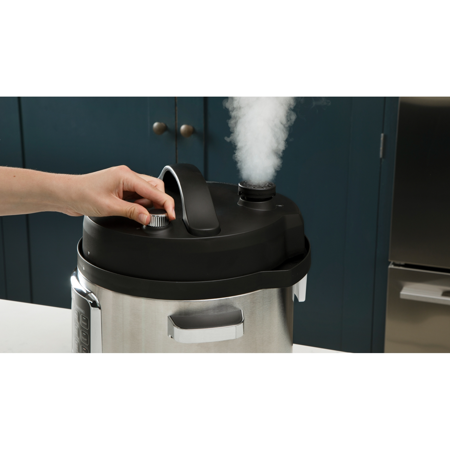 Una mano girando un dial en una olla a presión negra y plateada, sale vapor.