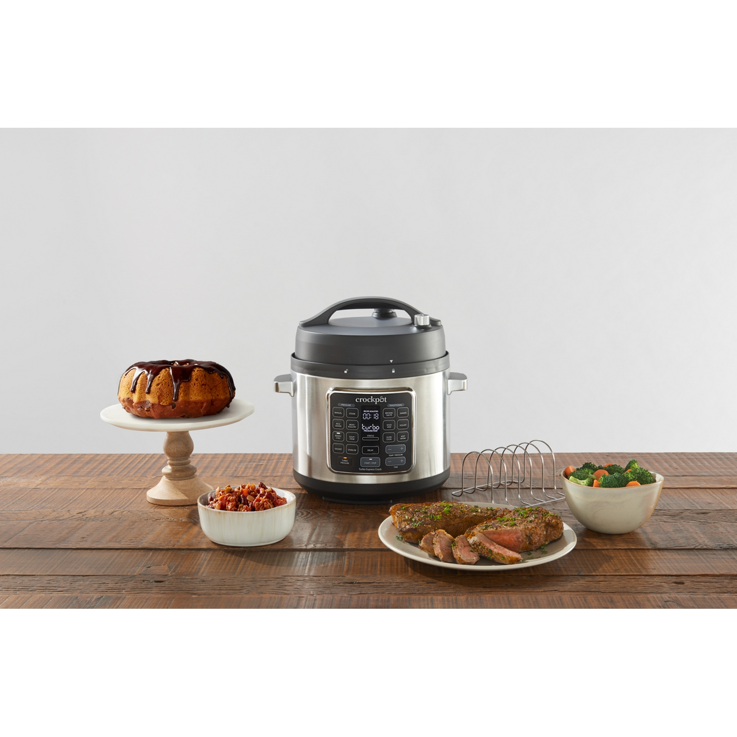 Una olla de cocción lenta con comida alrededor. Se ven pastel, verduras y carne.