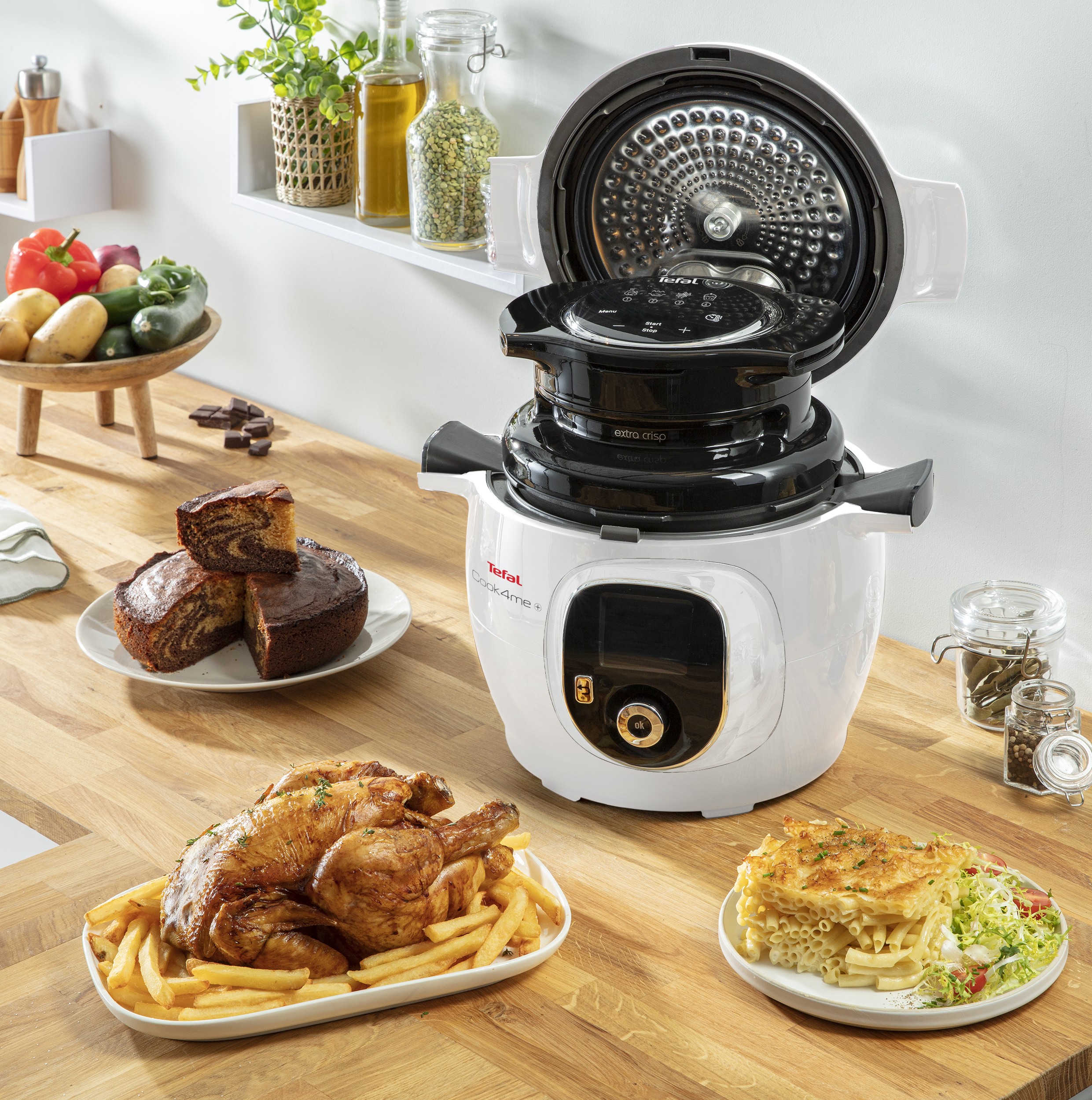 Tefal multifunkciós főzőgép ételekkel, mint sült csirke, sütemény és tészta az asztalon.
