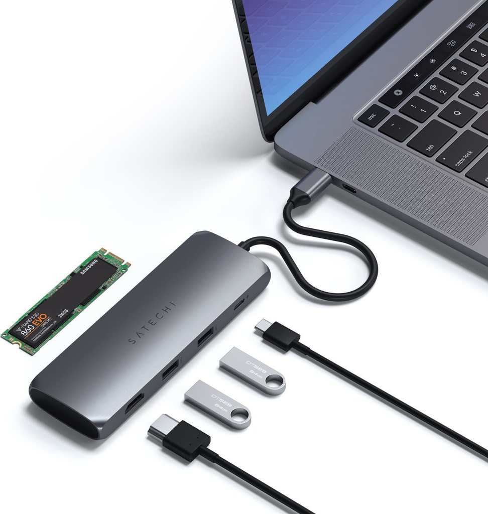 Un ordinateur portable connecté à un hub avec des disques SSD et USB. Le tout sur une surface blanche.