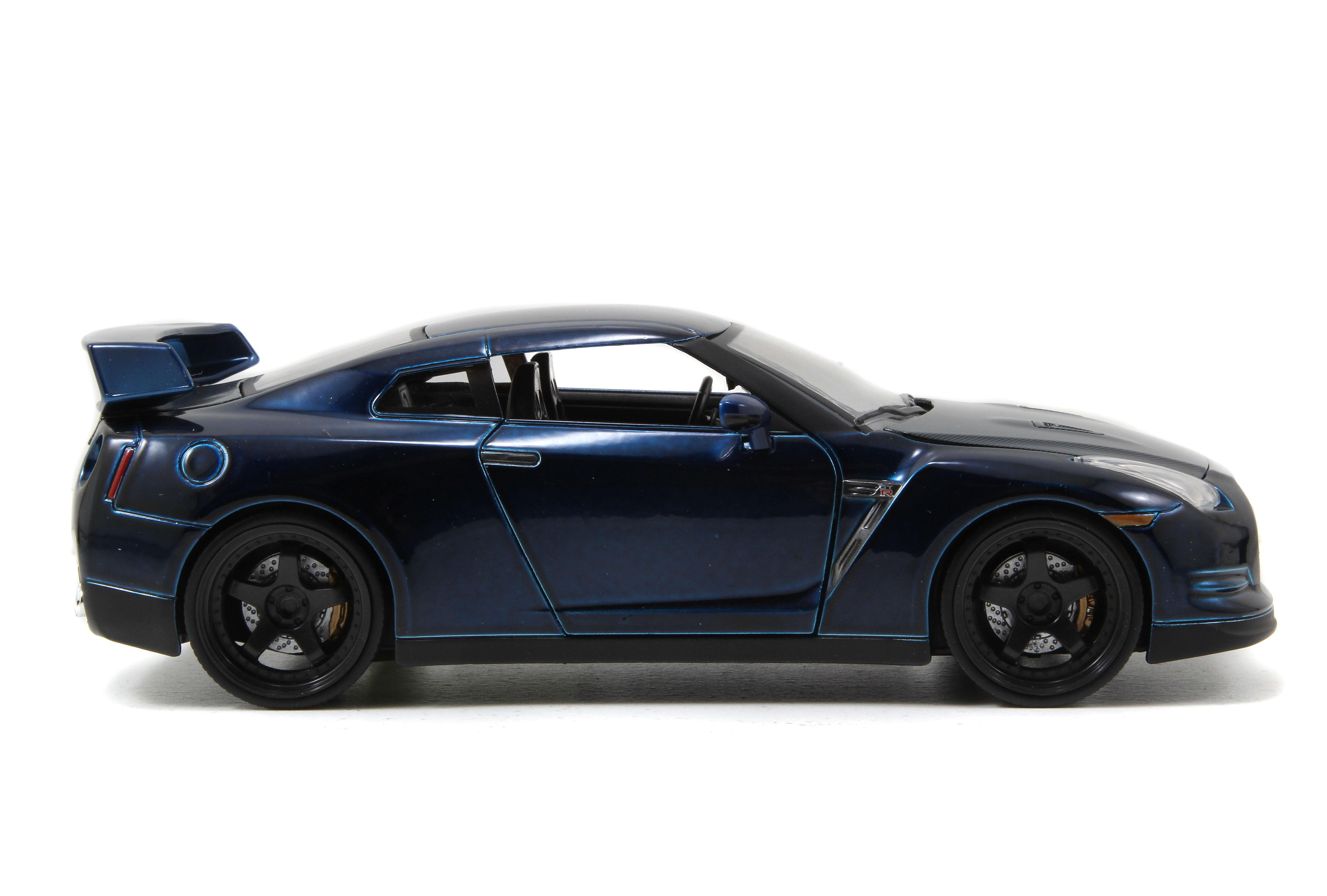 Ein blaues Sportwagenmodell steht auf weißem Untergrund. Das Auto hat schwarze Räder und einen Heckspoiler. Der Hintergrund ist weiß.