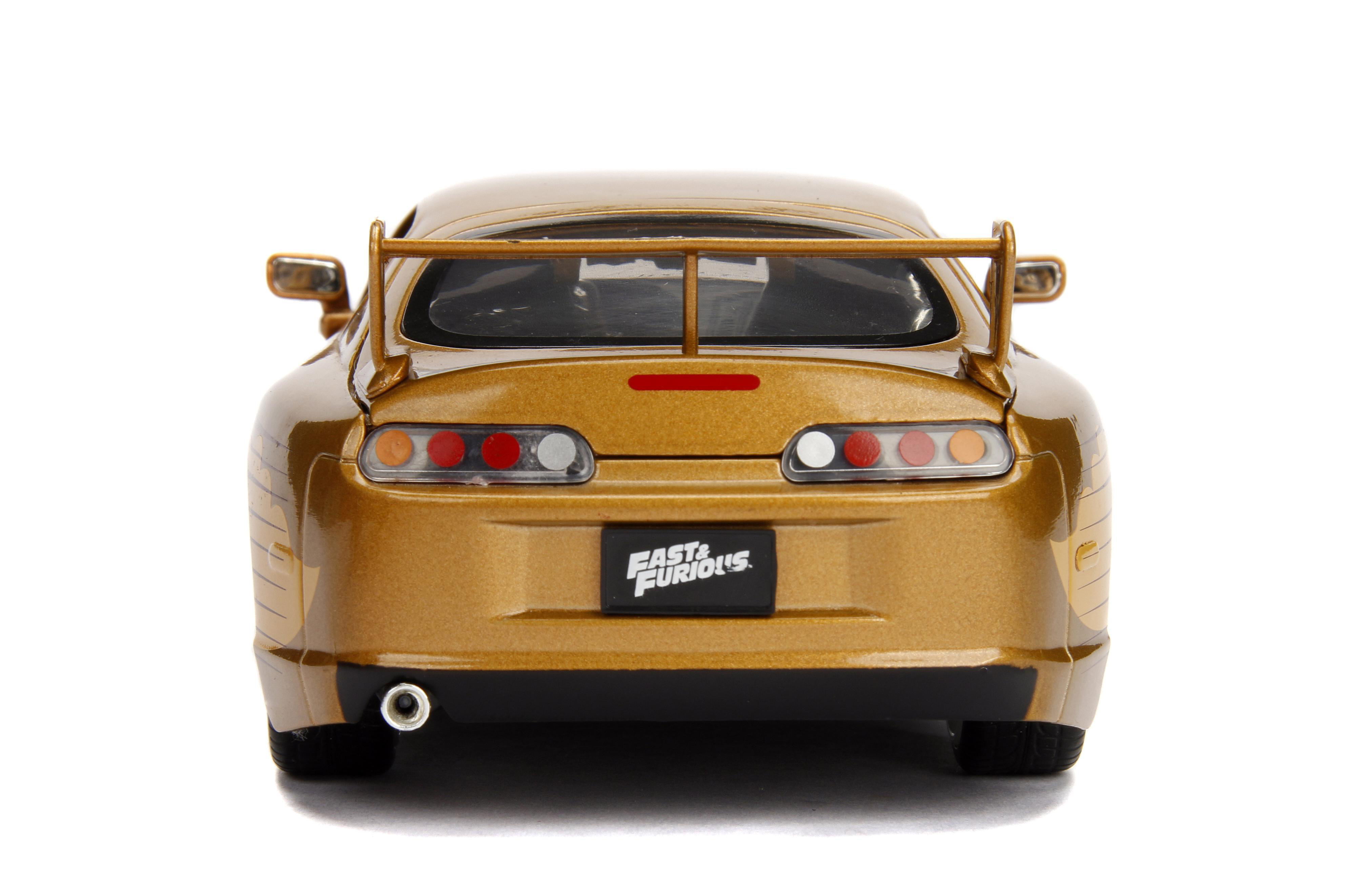 Ein goldfarbenes Spielzeugauto von hinten mit einem Spoiler. Es hat das Fast & Furious-Logo. Es steht auf weißem Grund.
