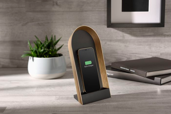 Un téléphone se rechargeant dans un support en bois, avec une plante, un livre et un cadre photo.