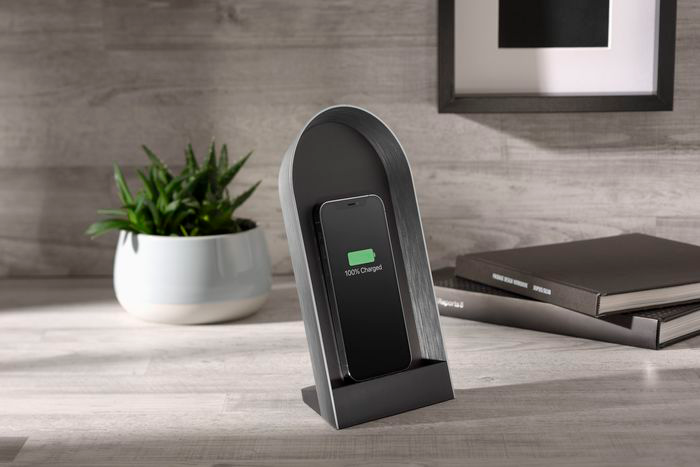 Station de charge avec téléphone. Écran affiche 100% chargé. Plante et livres.