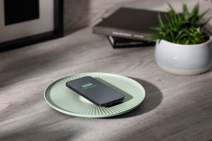 Smartphone se chargeant sans fil sur une assiette vert menthe, avec une plante et des livres en arrière-plan.