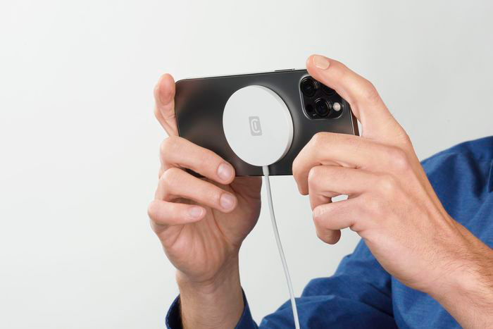 Person hält Telefon mit weißem kreisförmigen Ladegerät, Ladekabel.