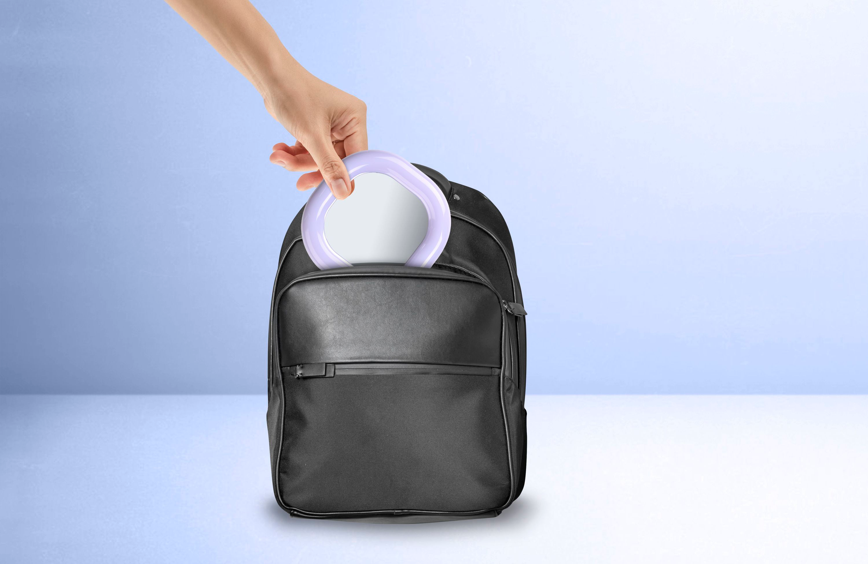 Hand legt Ringlicht in schwarzen Rucksack auf blau-weißem Hintergrund.