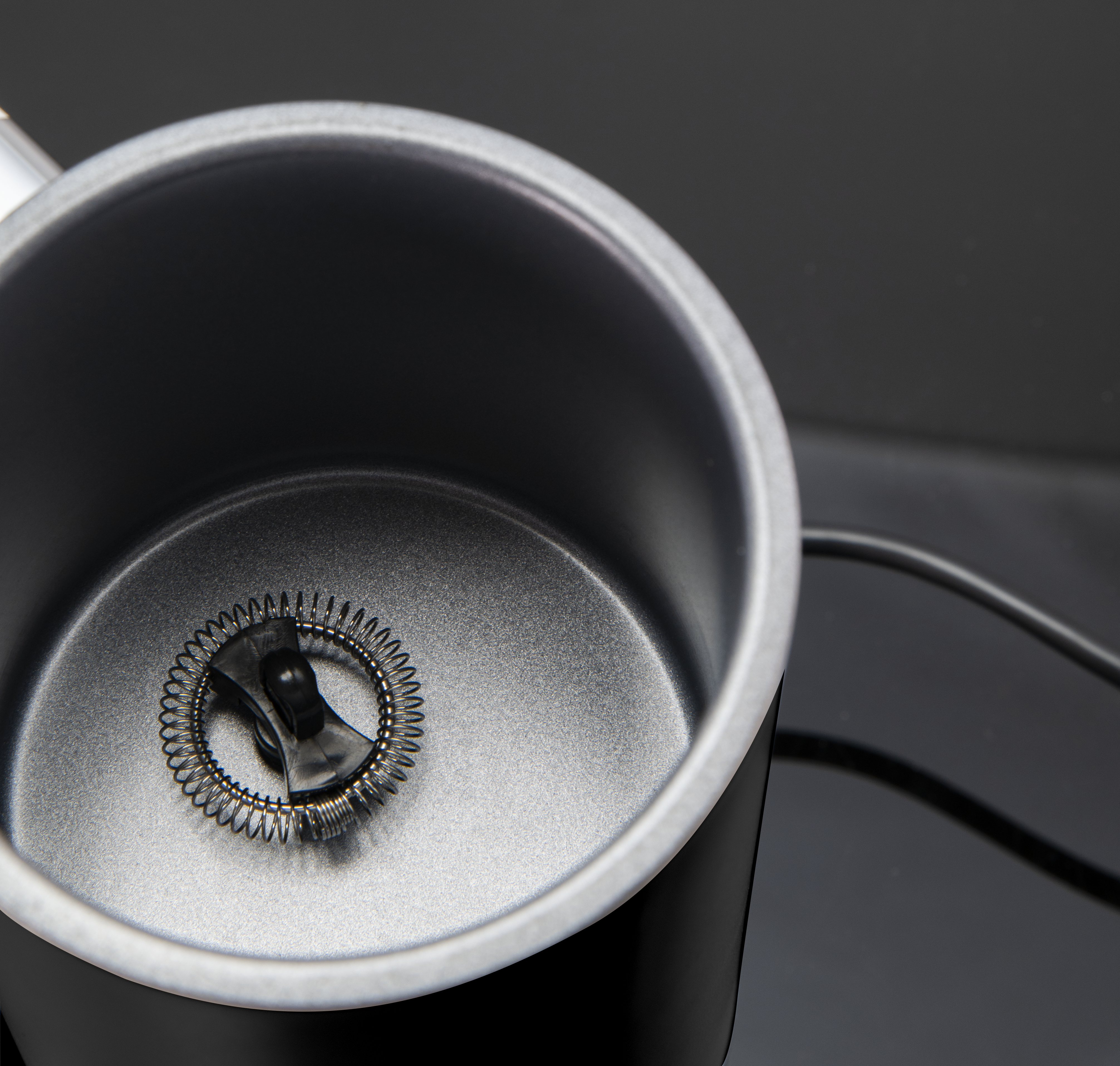 Ein schwarzer Milchaufschäumer. Die Innenseite der Tasse ist silber, und ein Schneebesen ist sichtbar.