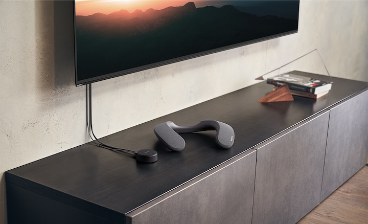 Fernseher auf dunklem Schrank. Soundbar und kleines schwarzes Gerät davor.