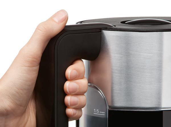 Hand hält schwarzen Griff eines silber-schwarzen Wasserkochers, Nahaufnahme.