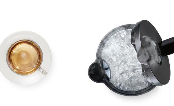 Eine Tasse Tee und ein dampfender Wasserkocher mit teilweise geöffnetem Deckel auf weißem Grund.