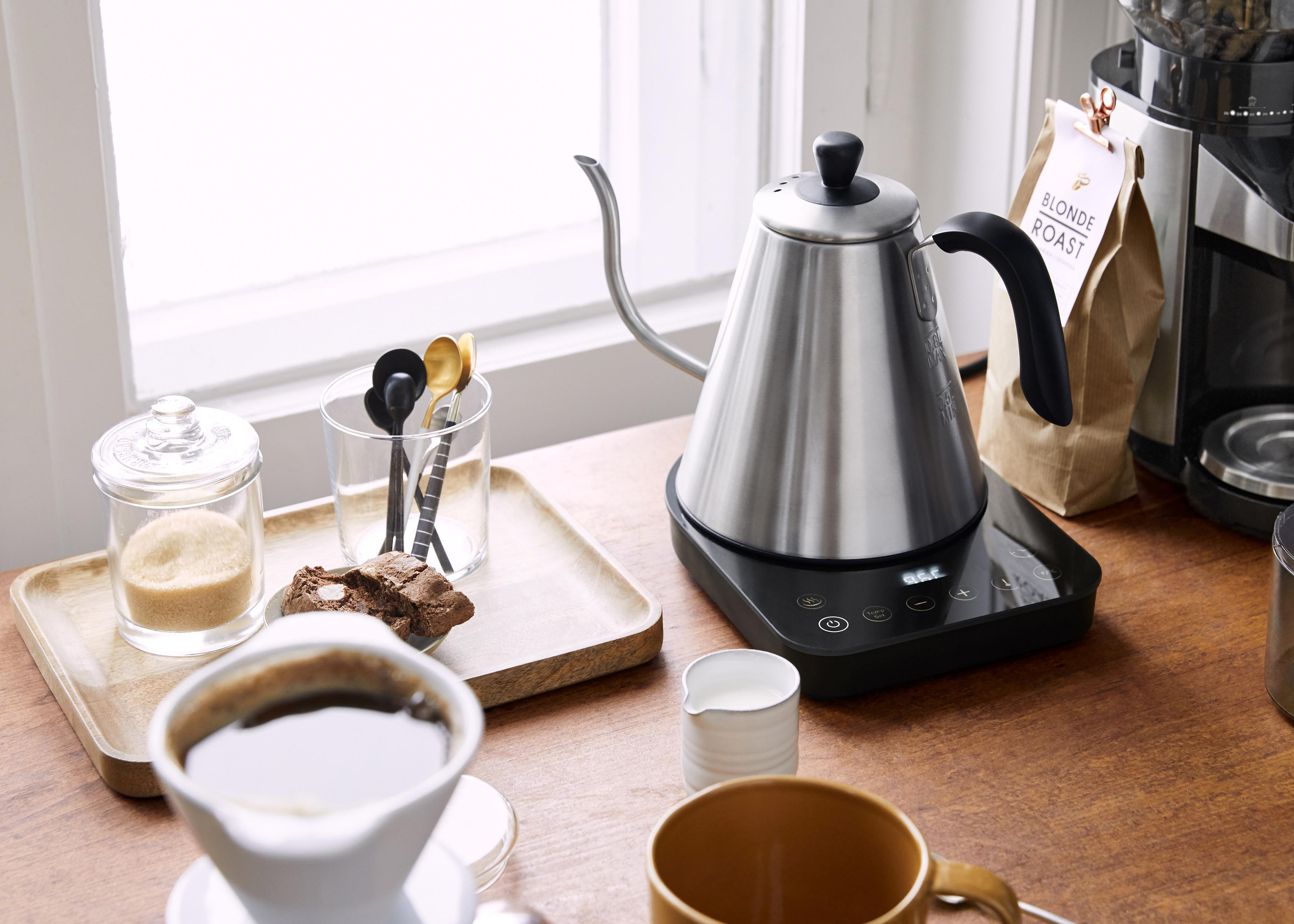 Kaffeezubereitung mit Wasserkocher und Zubehör auf einem Holztisch.