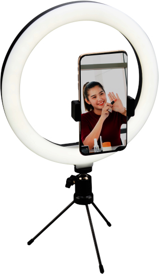 A woman in front of a ring light with a smartphone and beauty products on a tripod.
