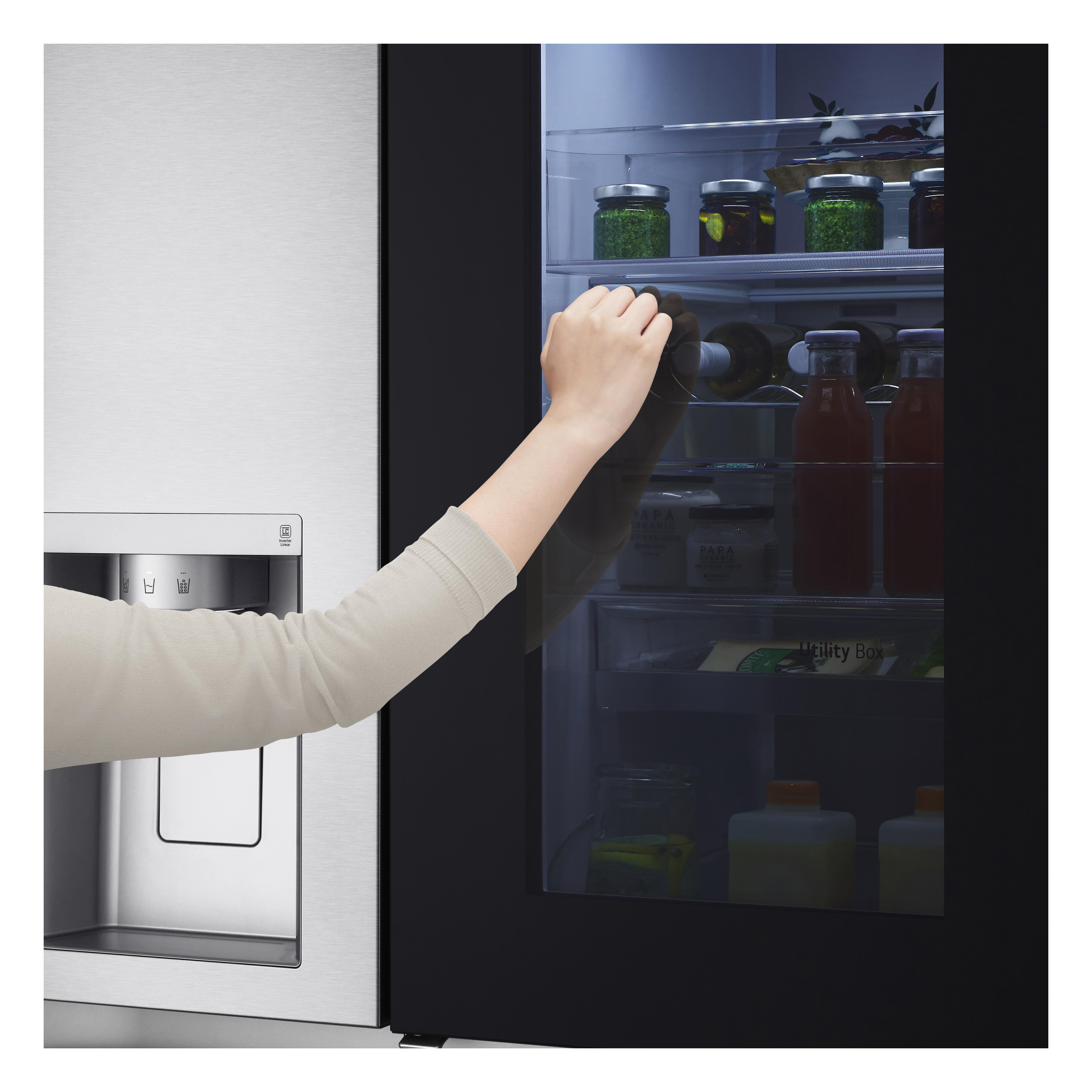 Die Hand einer Person greift in einen Kühlschrank, um eine Flasche zu nehmen. Im Kühlschrank befinden sich Gegenstände.
