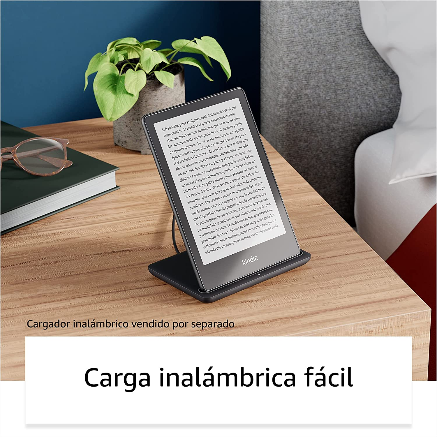 Una tableta en un soporte de carga, colocada sobre una mesa de madera junto a una planta y unas gafas.