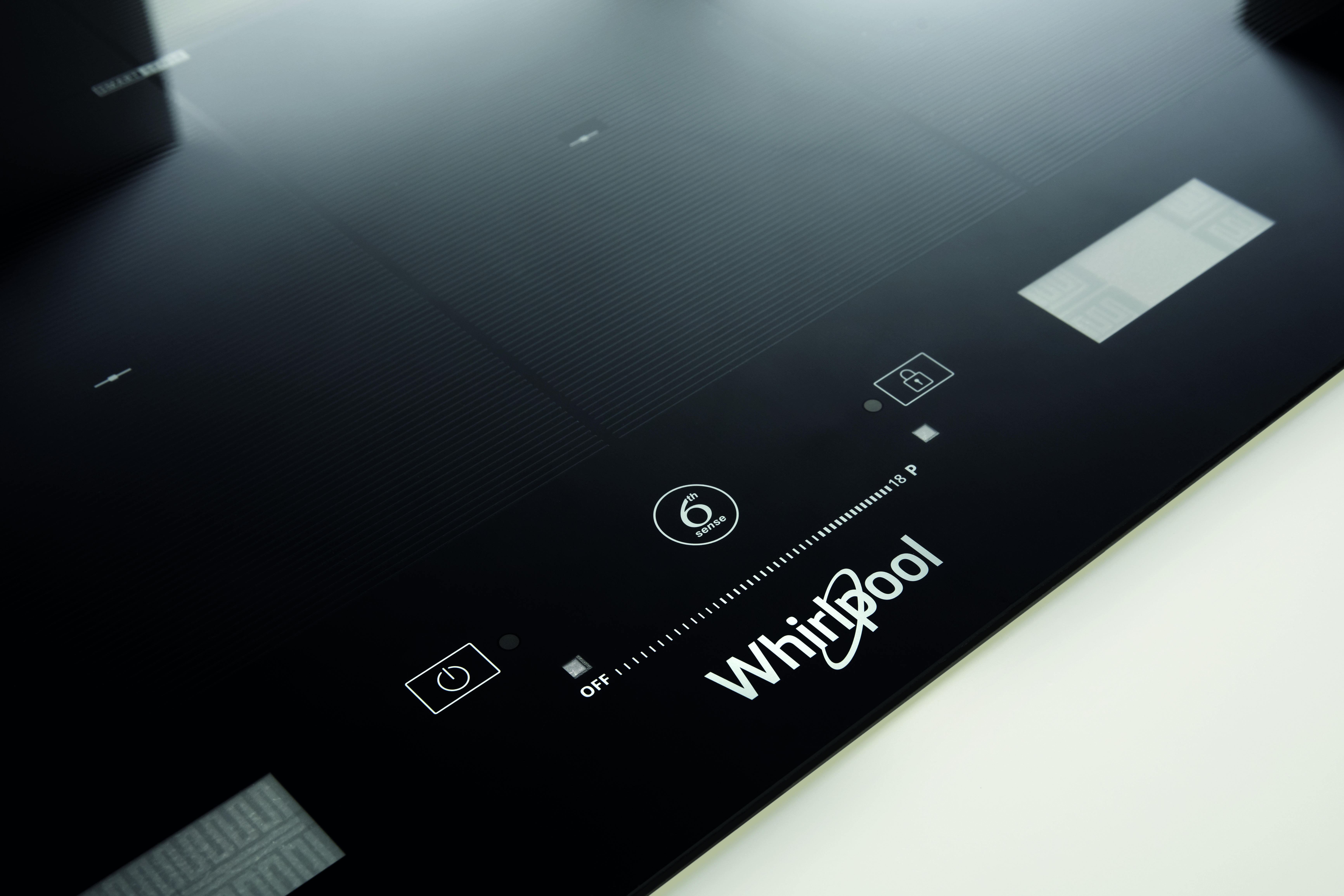 Fekete indukciós főzőlap közelképe Whirlpool logóval. Láthatók a bekapcsolás és a zár jelzői.