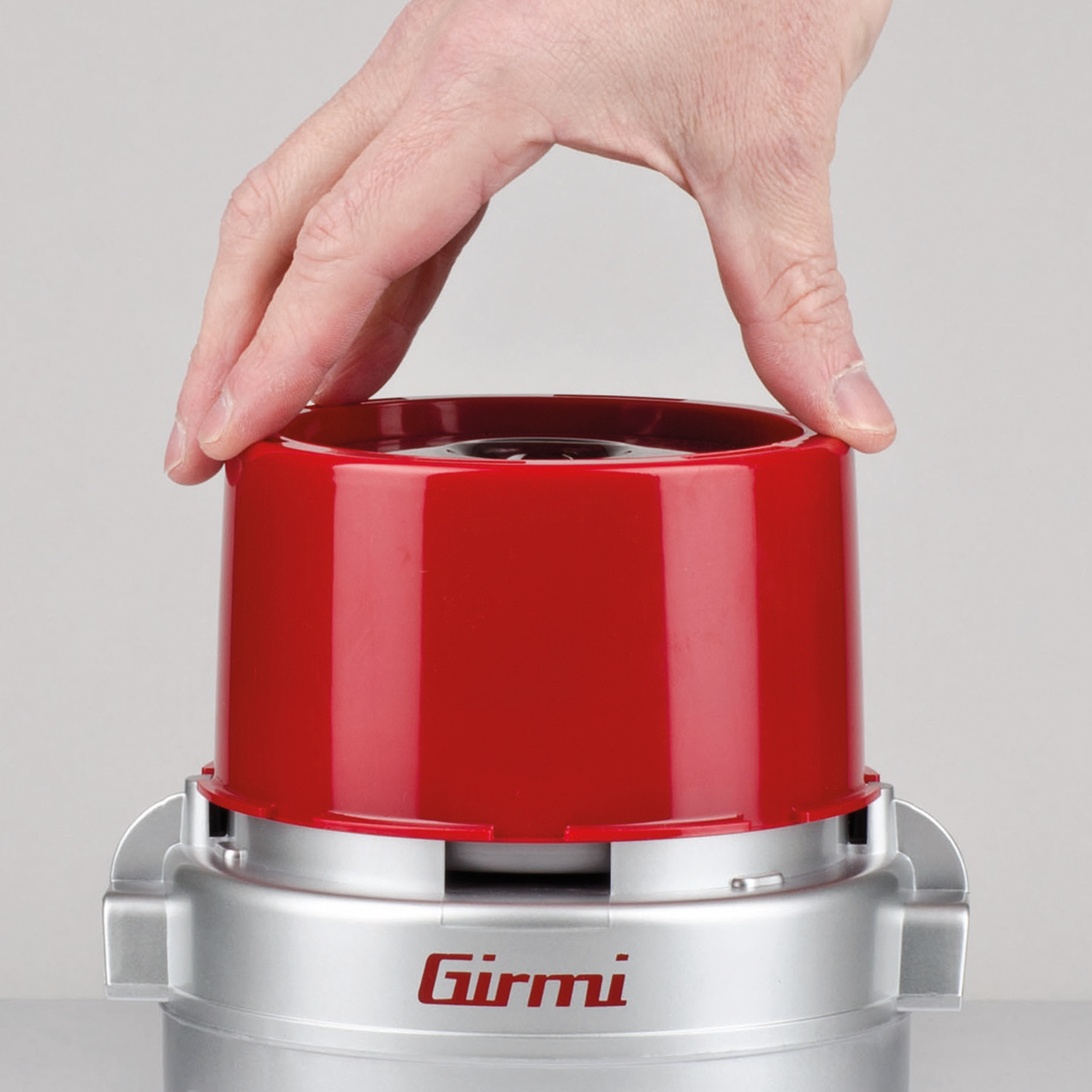 Mano che posiziona un coperchio rosso su una base argentata, con la scritta 'Girmi' sulla base.