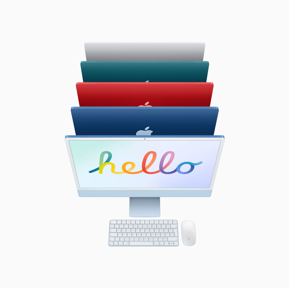 Gekleurde iMacs op elkaar. De voorste toont 'hello'. Toetsenbord, muis eronder. Kleuren: blauw, rood, groen en wit.