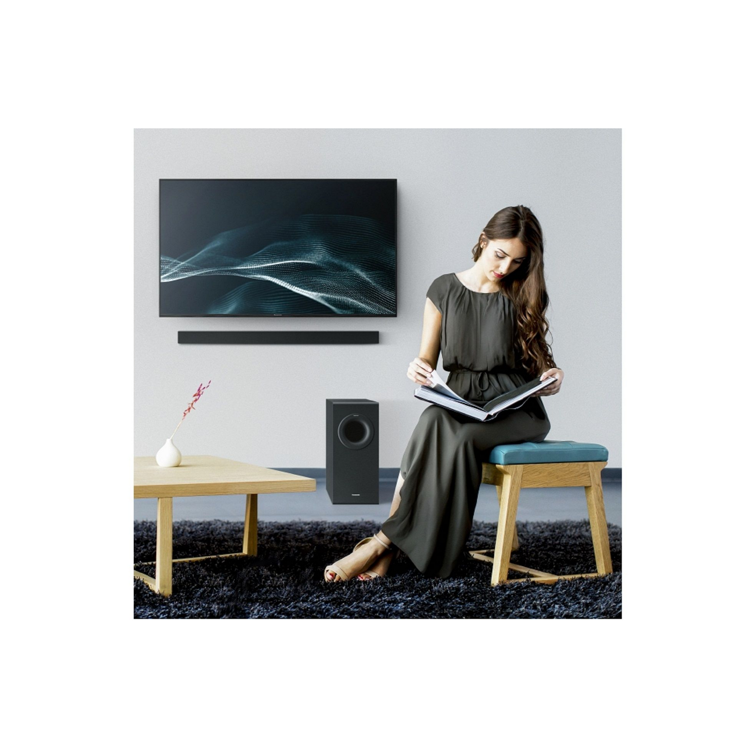 Una mujer leyendo un libro en una habitación con TV, barra de sonido, subwoofer y mesa de madera.