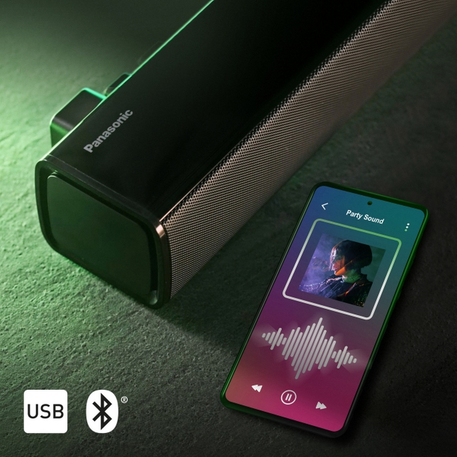 Barra de sonido negra con malla plateada y un smartphone que muestra una aplicación de música.