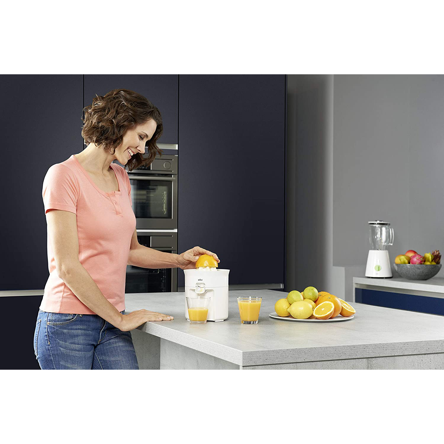 Donna che fa succo di arance con uno spremiagrumi in una cucina moderna.