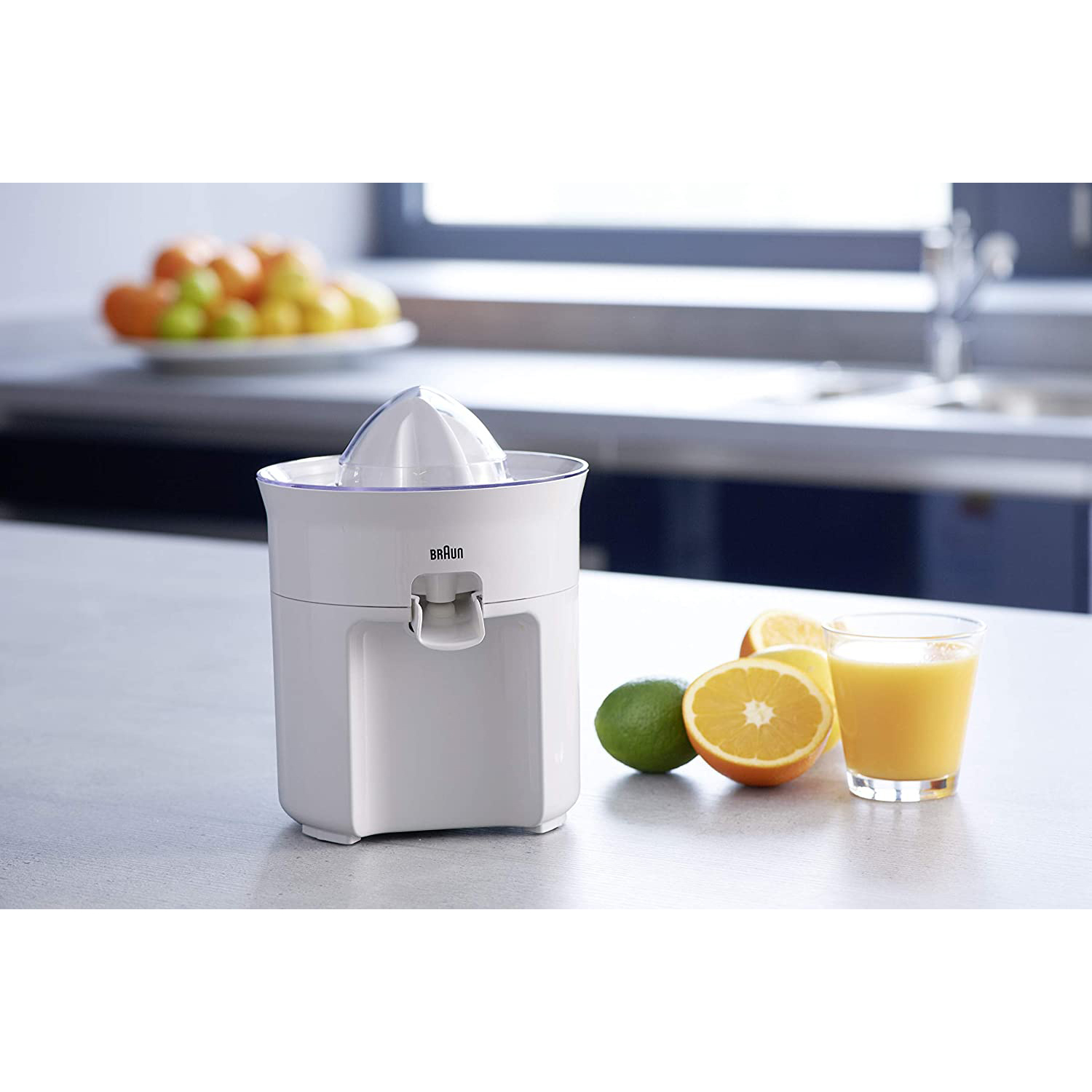 Spremiagrumi bianco con arance, lime e un bicchiere di succo.