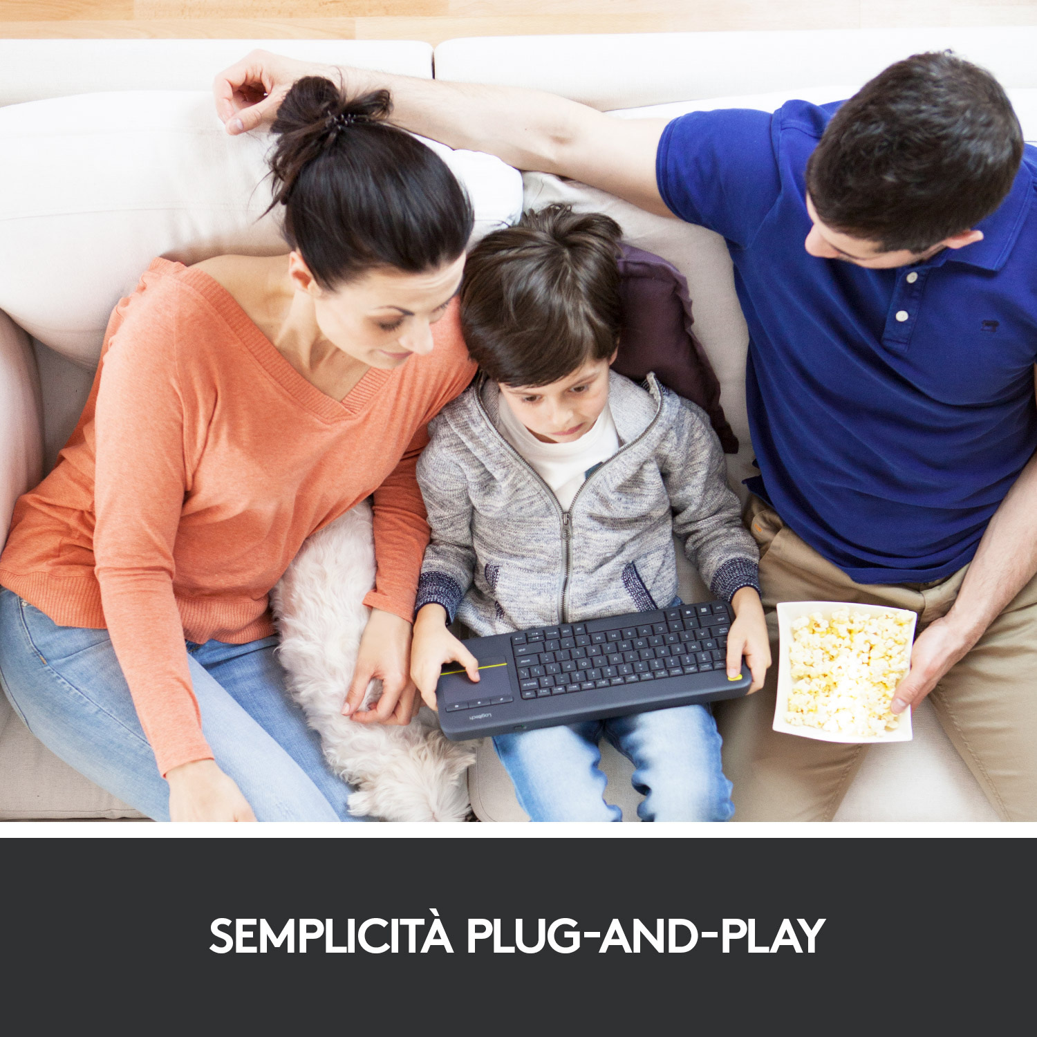 Famiglia sul divano. Il figlio tiene la tastiera, i genitori guardano. Popcorn sul tavolo.