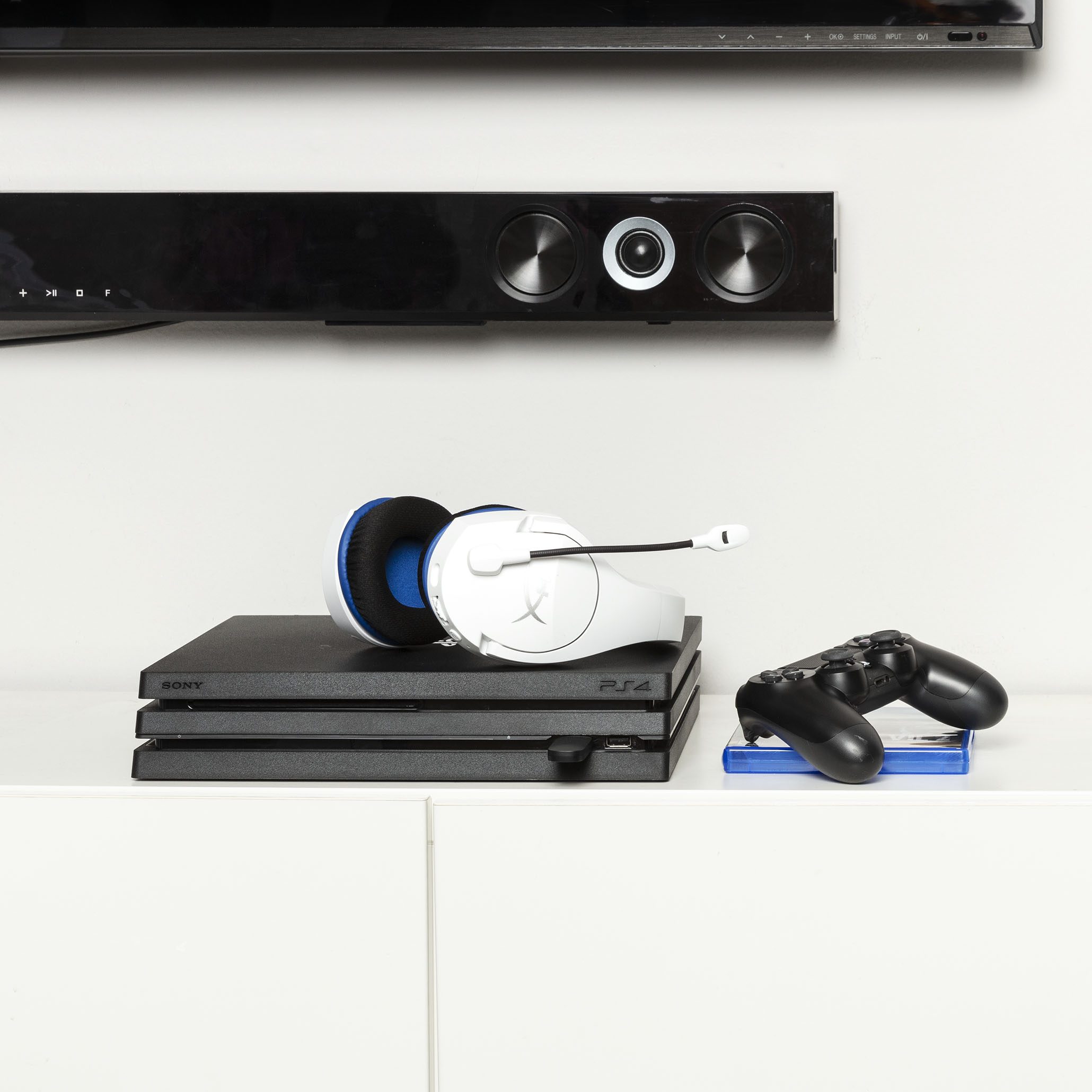 Schwarzes Gaming-Setup. Eine Konsole, Kopfhörer, Controller und eine Soundbar stehen auf einer weißen Oberfläche.