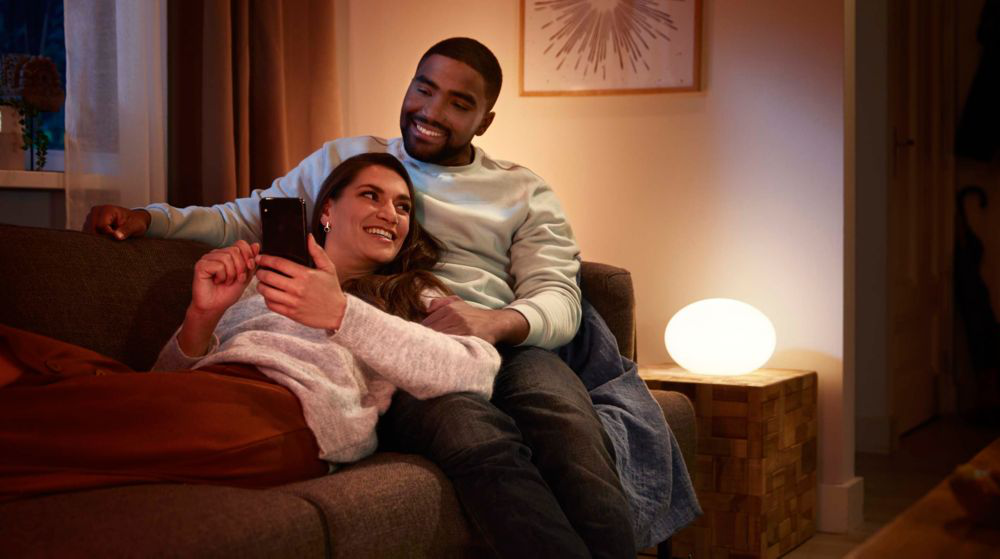 Un couple sur un canapé, la femme tient un téléphone, une lumière sur la table.
