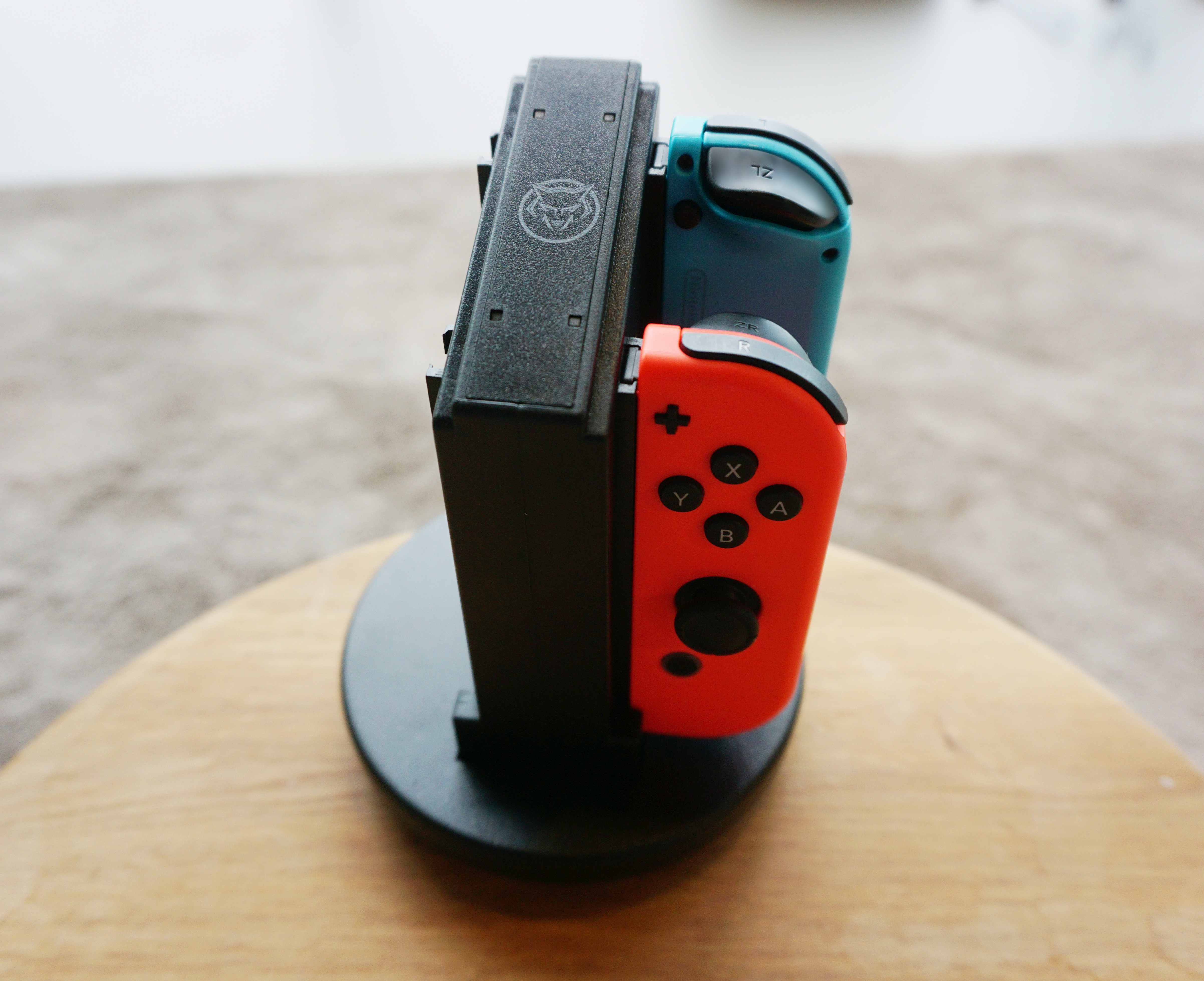 A stand with two game controllers: one blue and one red. On a wooden surface.