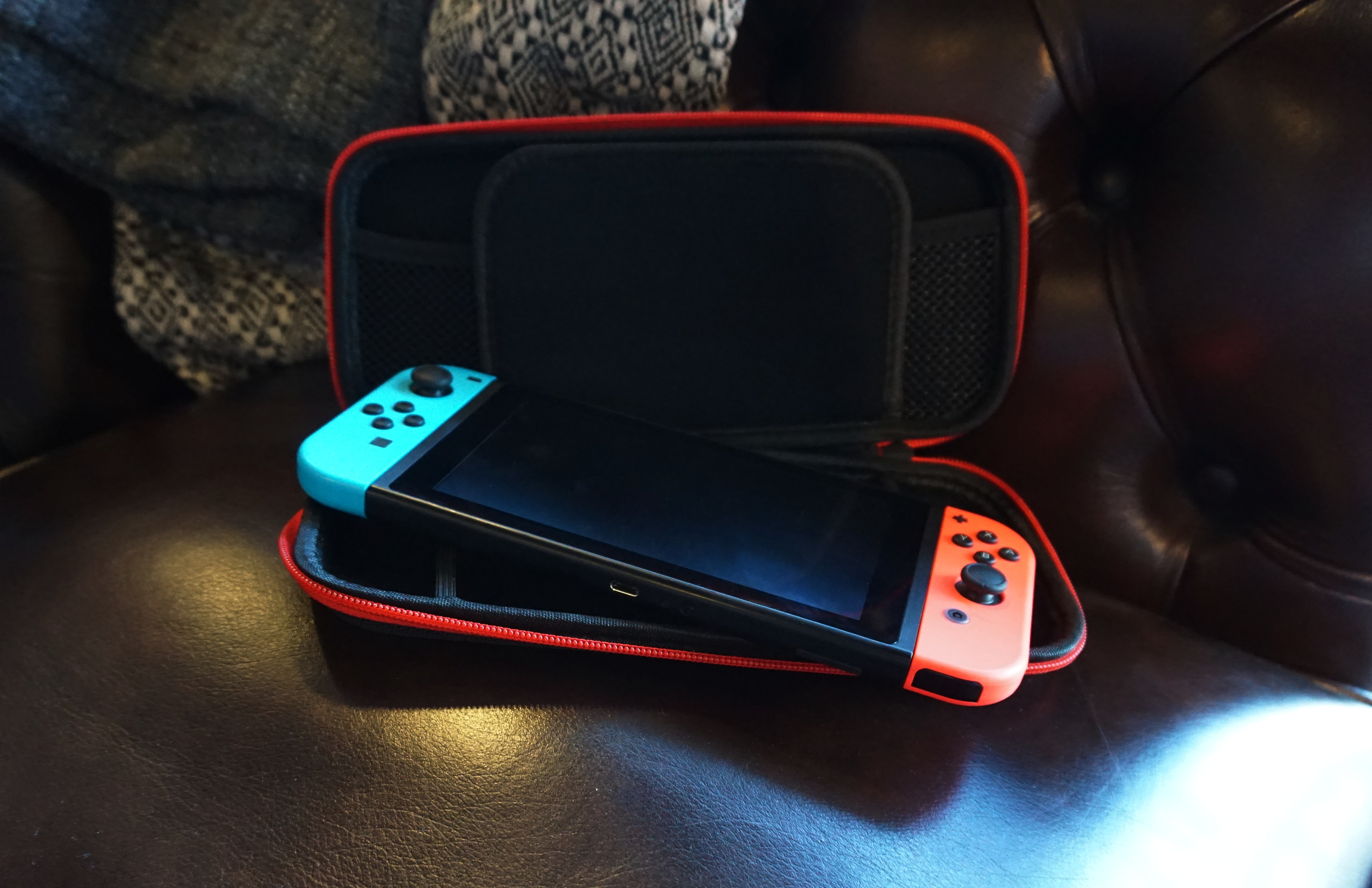 Nintendo Switch with red and blue controllers in a red and black case on a brown leather surface.