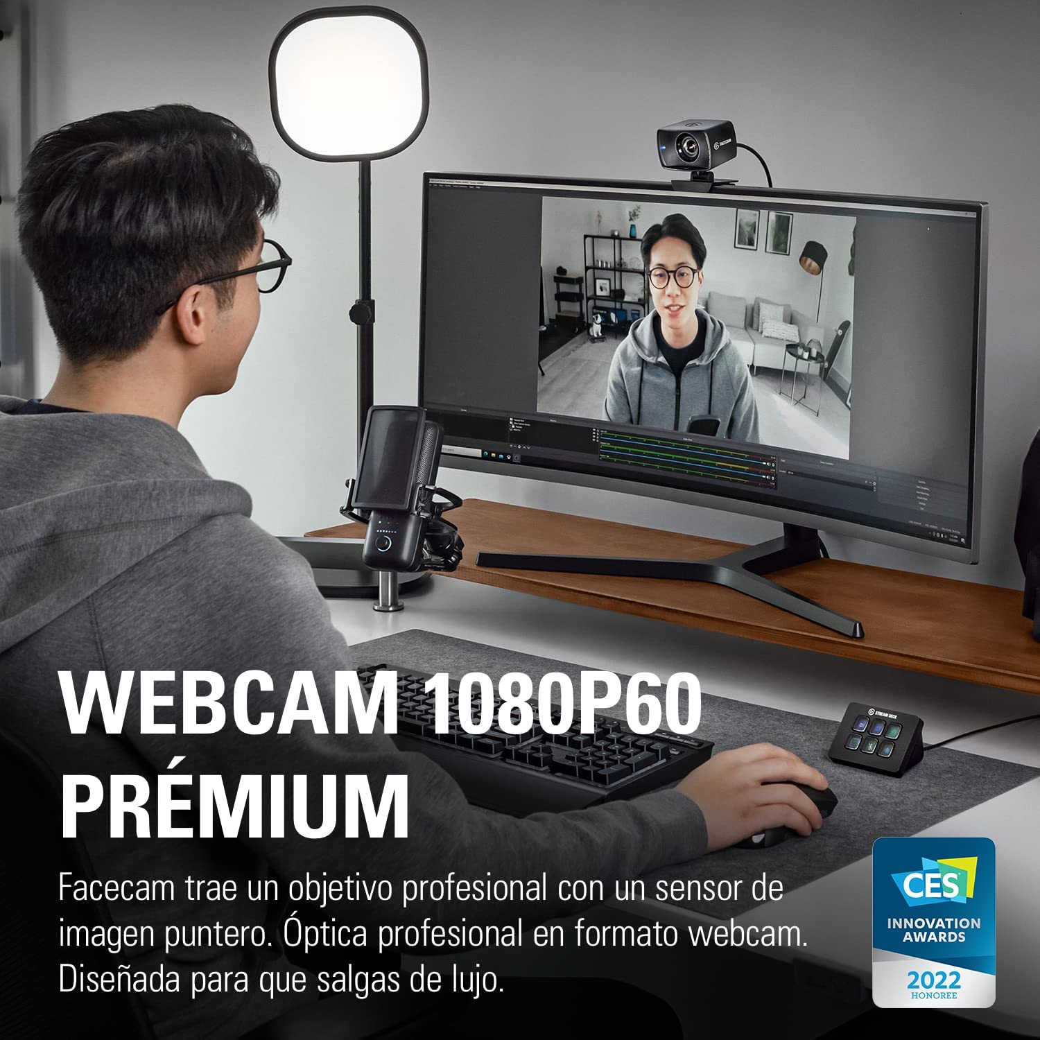 Hombre usando webcam, monitor mostrando videollamada y teclado.