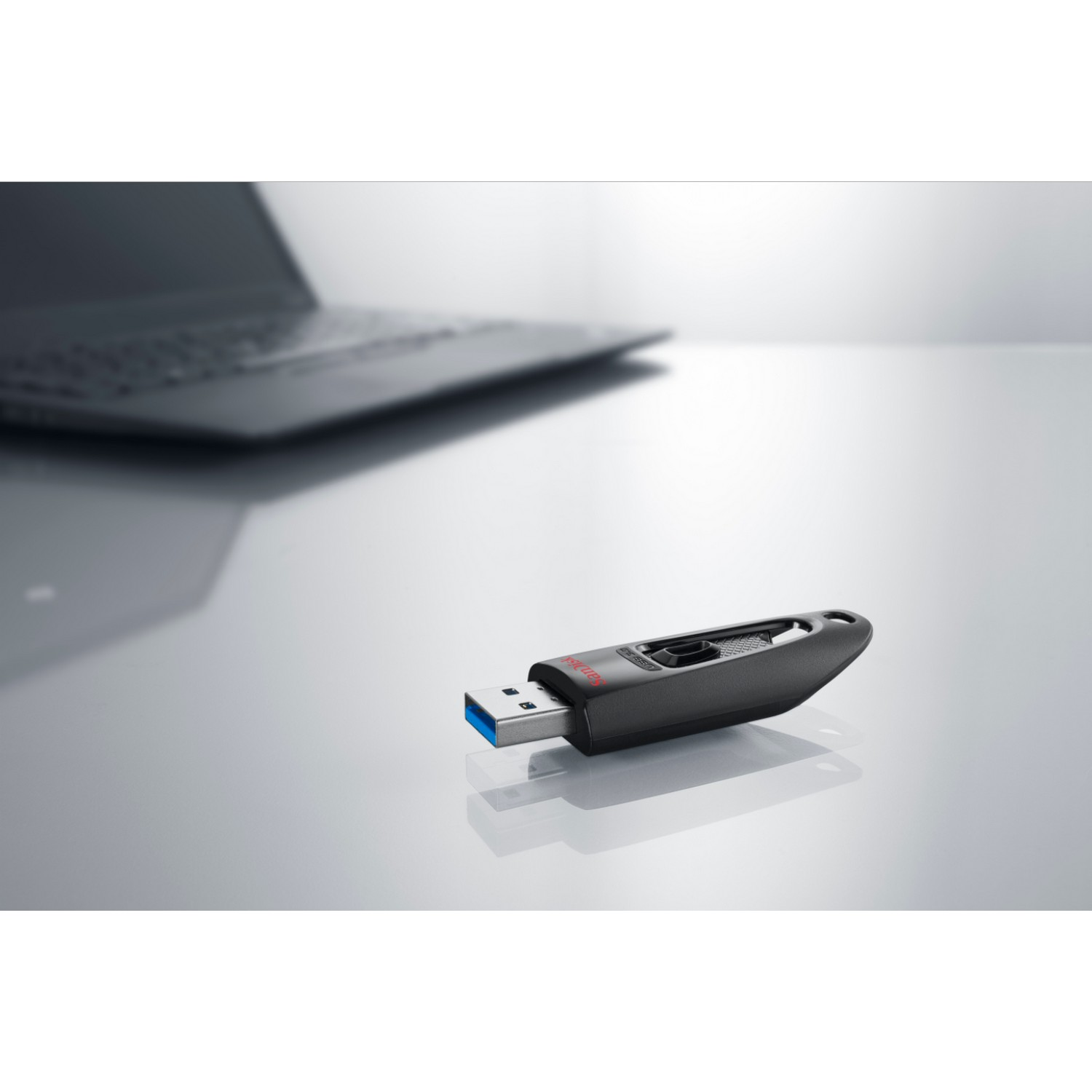 Memoria USB negra sobre una superficie brillante y clara con un portátil al fondo.